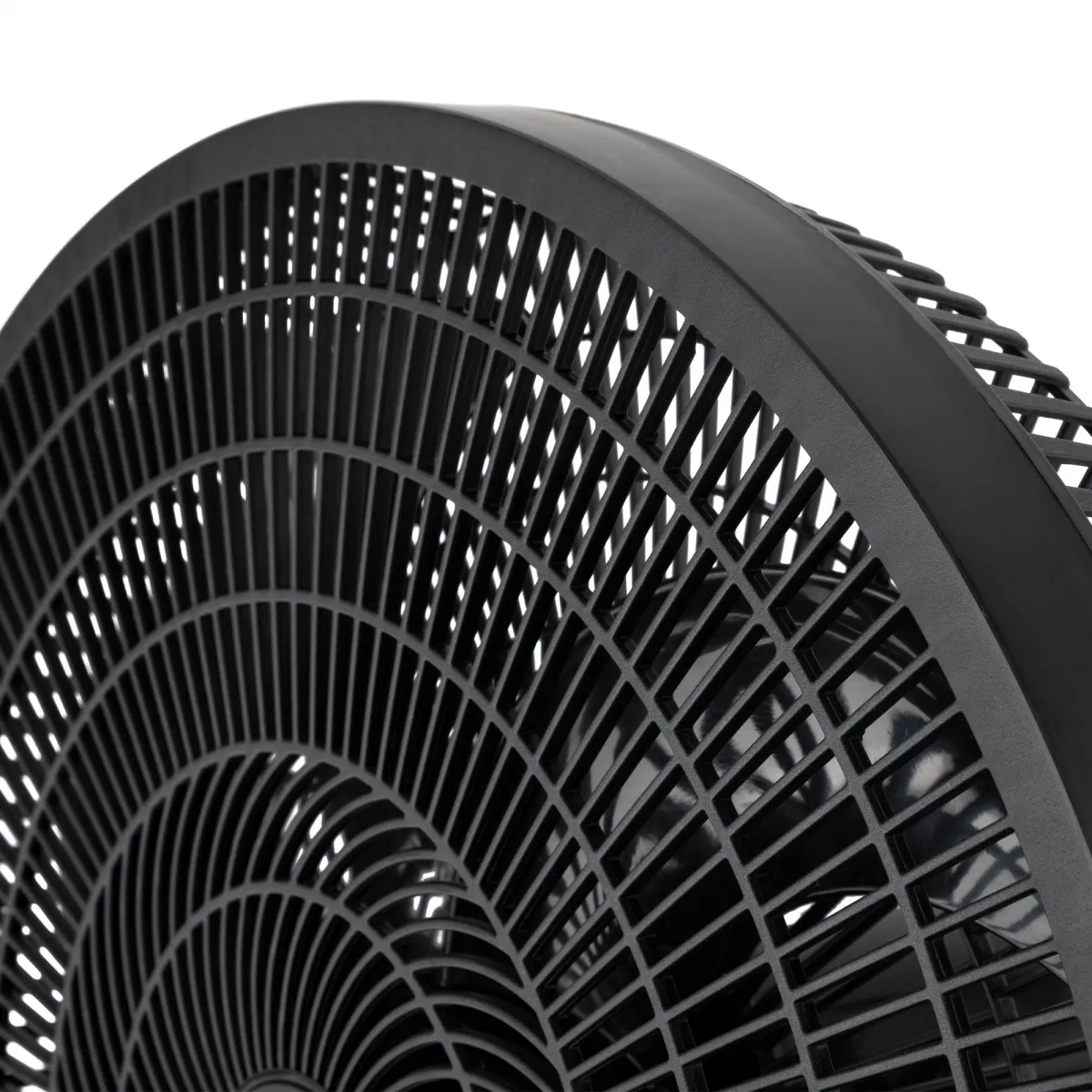 Primer plano de un ventilador negro. El ventilador tiene una cubierta frontal curva y enrejada. Las aspas son visibles detrás de la cubierta. Fondo blanco.