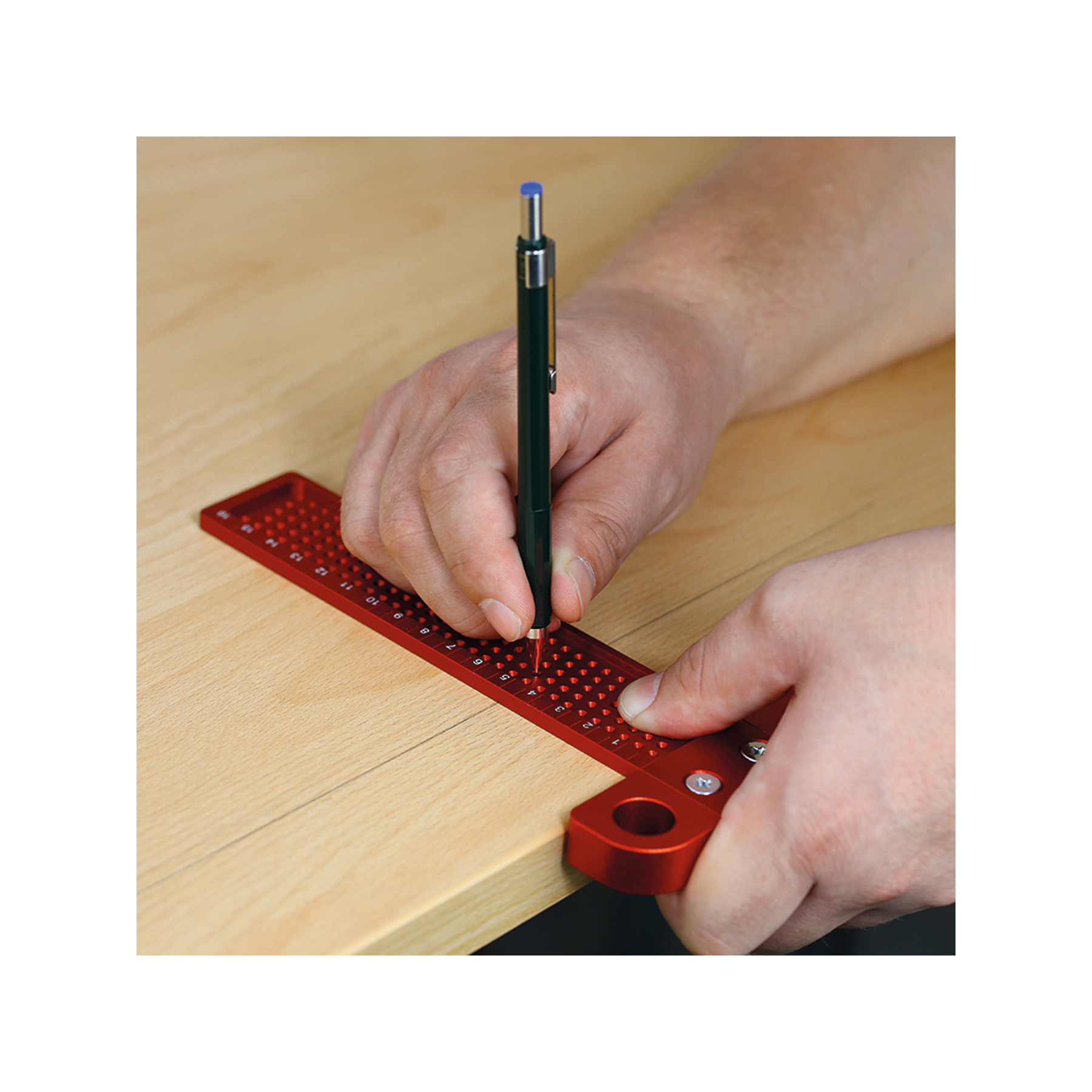 Hände, die ein rotes Quadrat verwenden, um mit einem schwarzen Stift eine Linie auf Holz zu messen und zu zeichnen. Der Stift hat eine blaue Spitze.