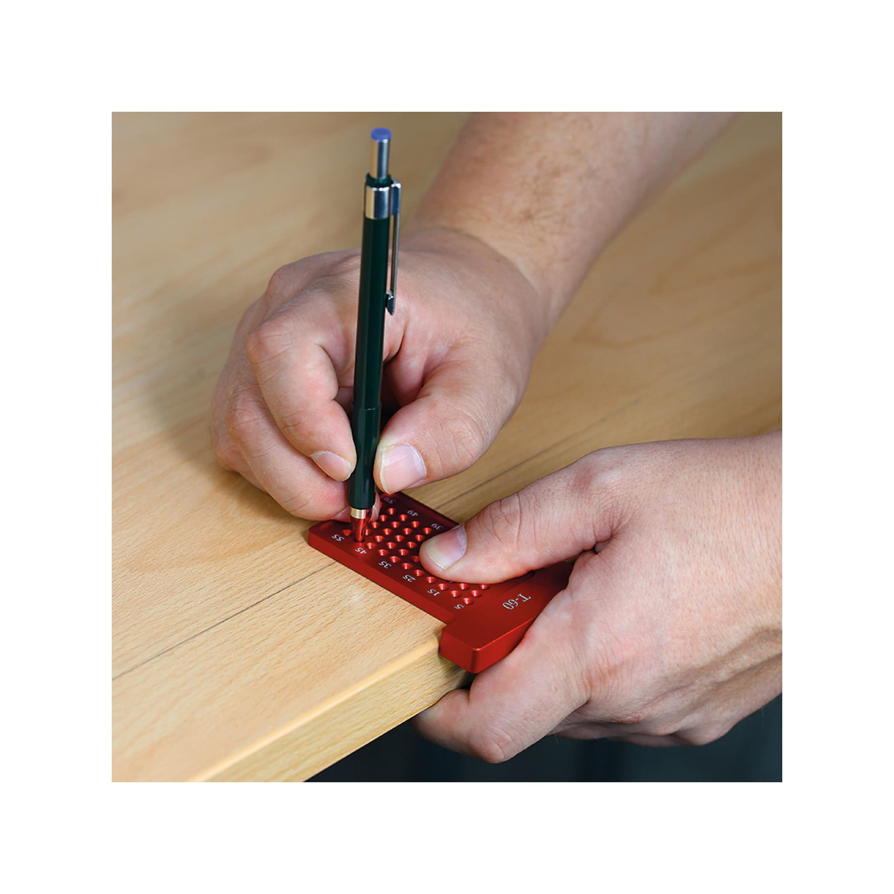 Hände, die einen Bleistift und ein rotes T-Quadrat verwenden, um eine Holzoberfläche zu markieren. Der Bleistift ist grün und das Quadrat hat Messungen.