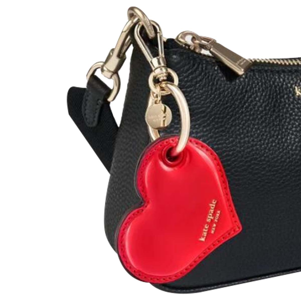 Ein roter herzförmiger Kate Spade-Schlüsselanhänger hängt an einer schwarzen Tasche. Der Schlüsselanhänger hat goldfarbene Hardware.