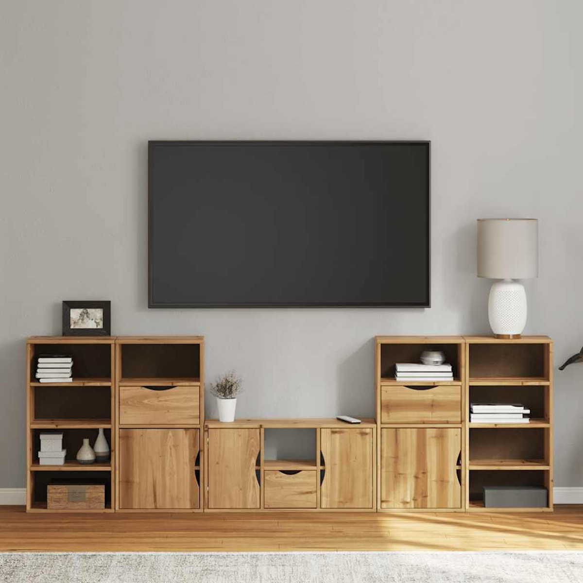 Ein Wohnzimmer mit großem Fernseher, Holzschränken, einer Lampe und einem Teppich. Die Wand ist grau, der Boden ist aus Holz.