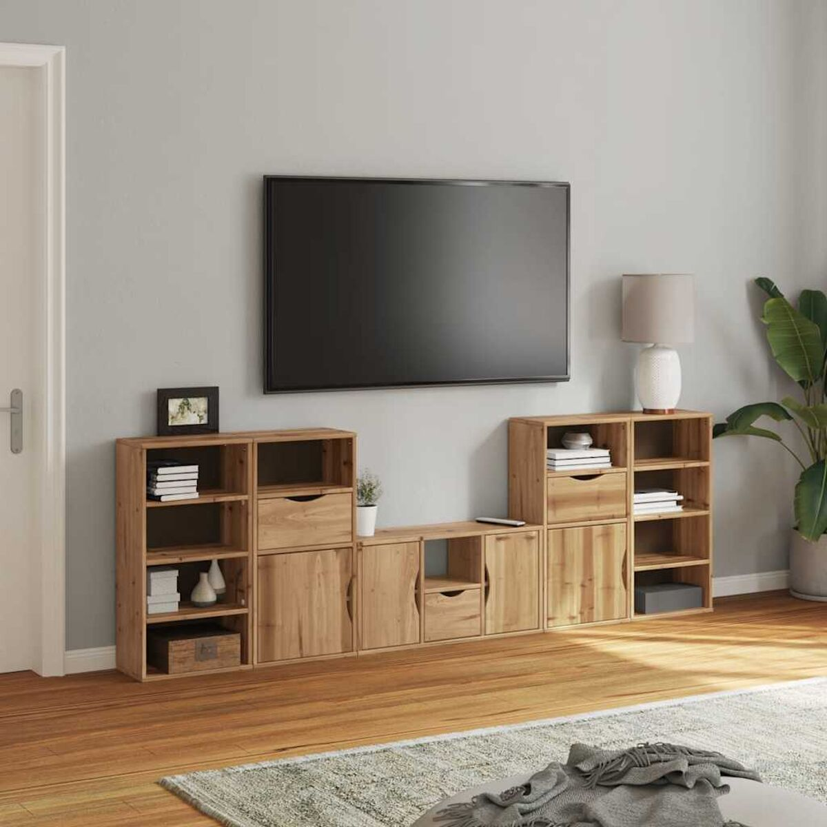 Wohnzimmer mit Fernseher, Holzregalen, Lampe und Pflanze. Bücher, Dekoration und ein Teppich sind sichtbar. Tür links.
