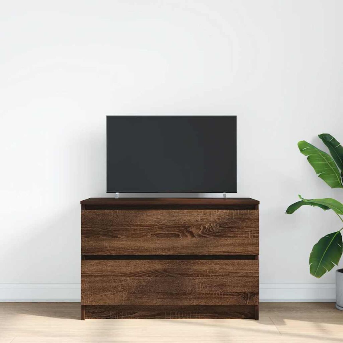 Eine Holzkommode mit einem Fernseher darauf. Rechts von der Kommode befindet sich eine Pflanze.