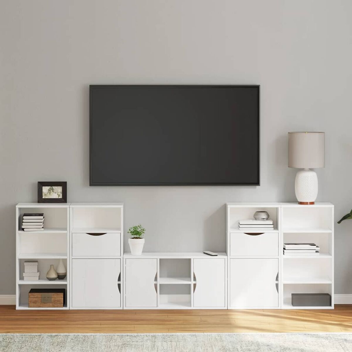 Modernes Wohnzimmer mit großem Fernseher, weißen Schränken, Lampe und Pflanze auf Holzboden. Graue Wand.