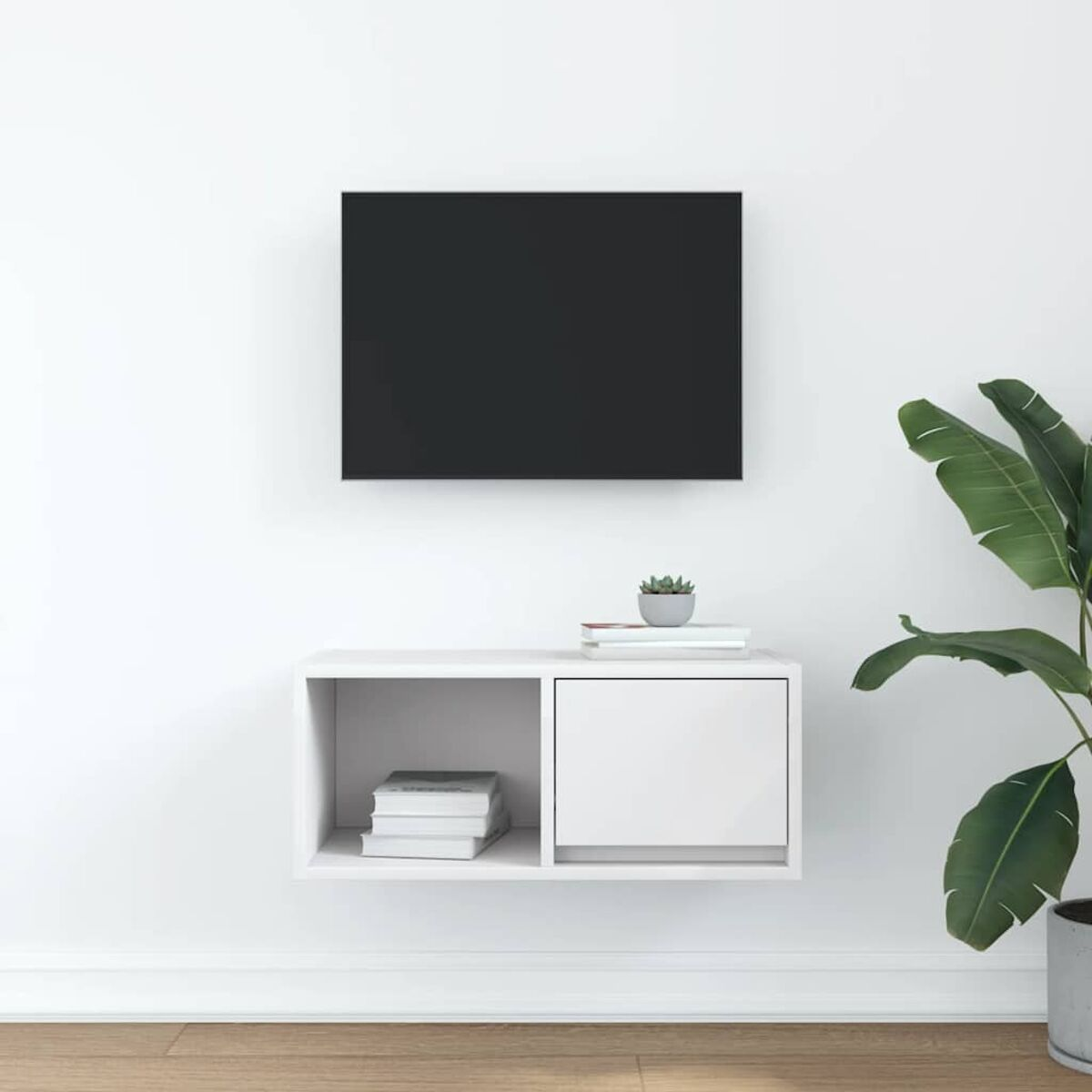 Ein schwarzer Fernseher hängt über einem weißen, an der Wand befestigten Schrank. Rechts ist eine Pflanze mit großen grünen Blättern.