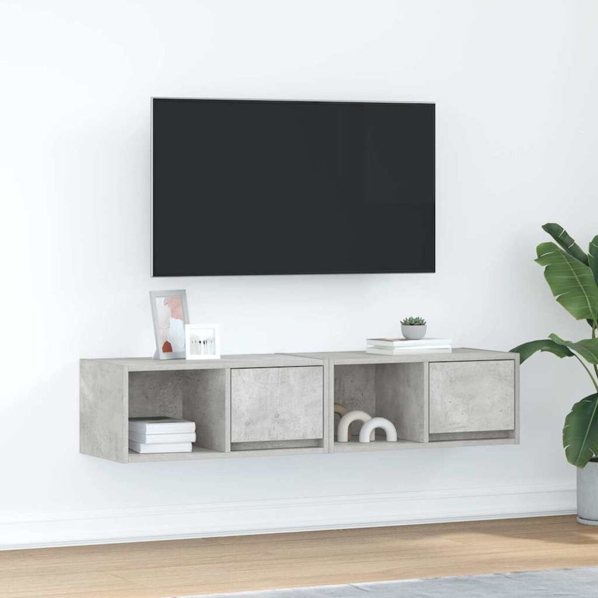 Ein wandmontierter Fernseher mit einem grauen schwebenden Regal darunter. Das Regal hat Bücher, Dekorationsgegenstände und eine kleine Pflanze.