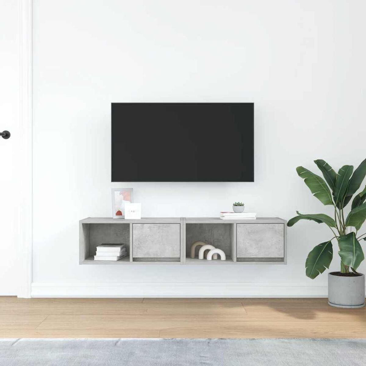 Ein modernes Wohnzimmer. Ein Fernseher ist an einer weißen Wand über einem grauen schwebenden Schrank angebracht. Rechts steht eine Topfpflanze.