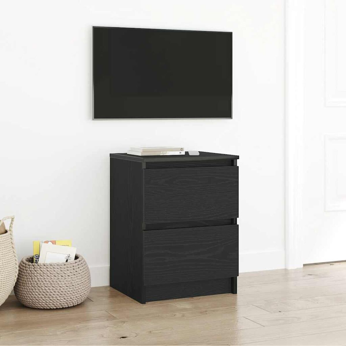 Ein schwarzer Schrank mit zwei Schubladen steht unter einem großen Fernseher. Links sind ein geflochtener Korb und Bücher.