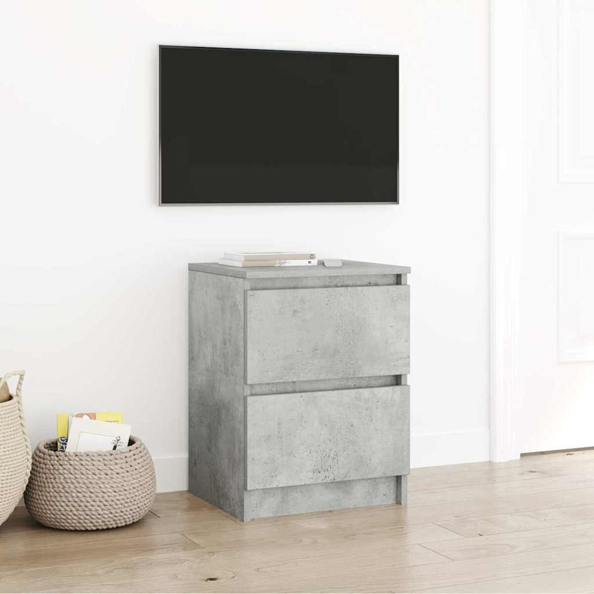 Ein grauer Beton-Schrank mit zwei Schubladen steht unter einem montierten Fernseher. Links ist ein geflochtener Korb. Bücher liegen auf dem Schrank.