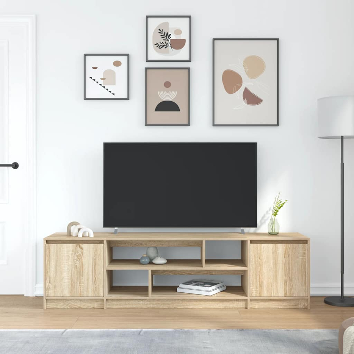 Wohnzimmerszene mit Fernseher, Holzschrank, Kunstdrucken und Stehlampe. Neutrale Farben dominieren den Raum.
