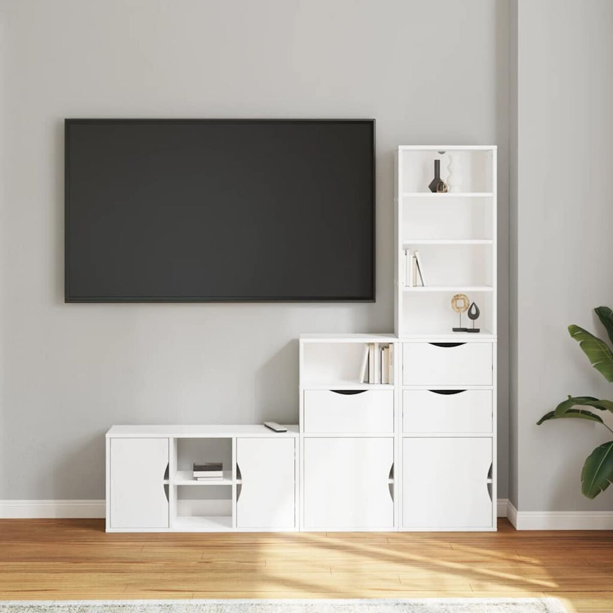 Ein Wohnzimmer mit großem Fernseher, weißen Aufbewahrungseinheiten und einem Bücherregal. Rechts steht eine Pflanze. Holzfußboden.