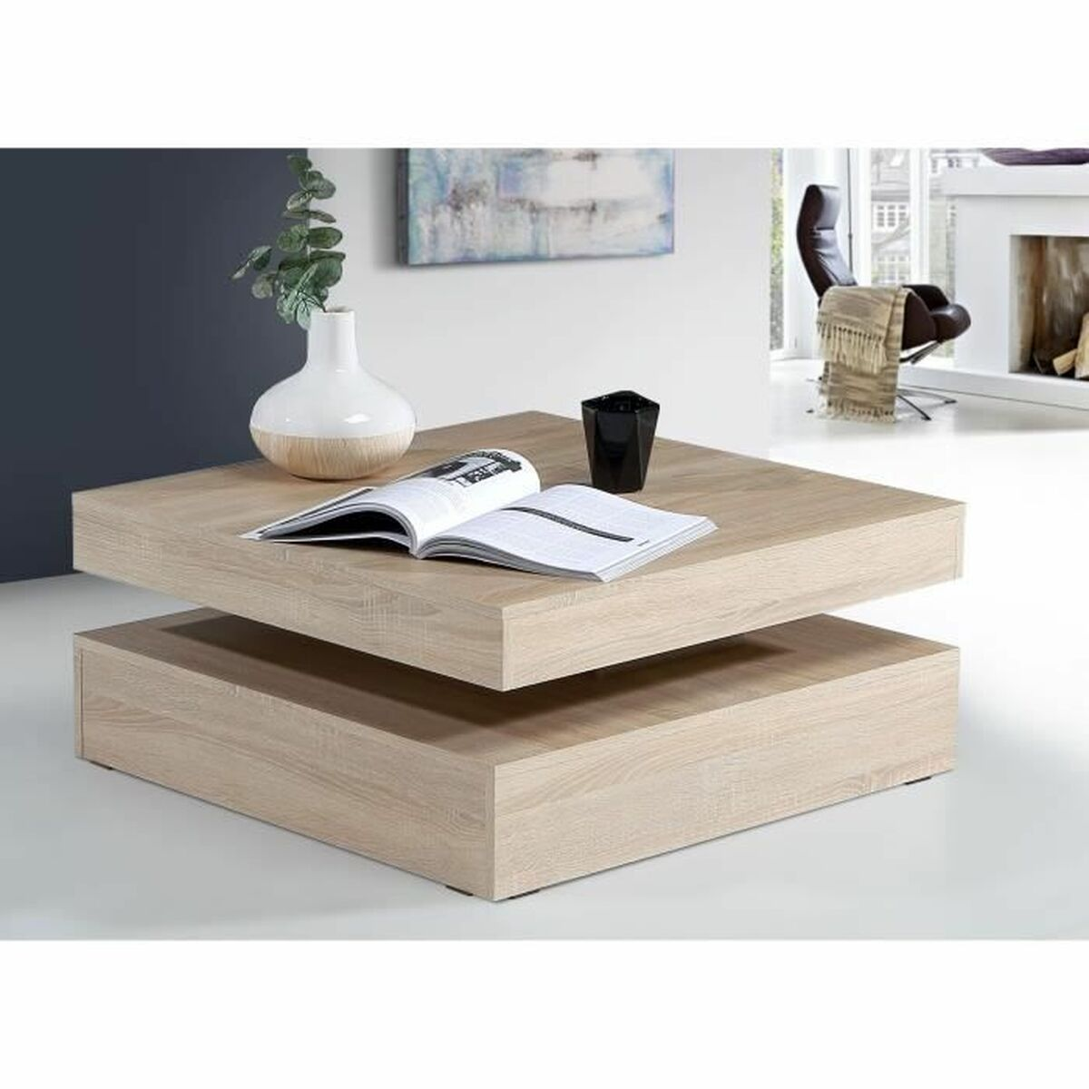 Ein zweistufiger Couchtisch aus Holz mit Vase, Buch und schwarzem Becher. Ein Stuhl und ein Kamin sind im Hintergrund.