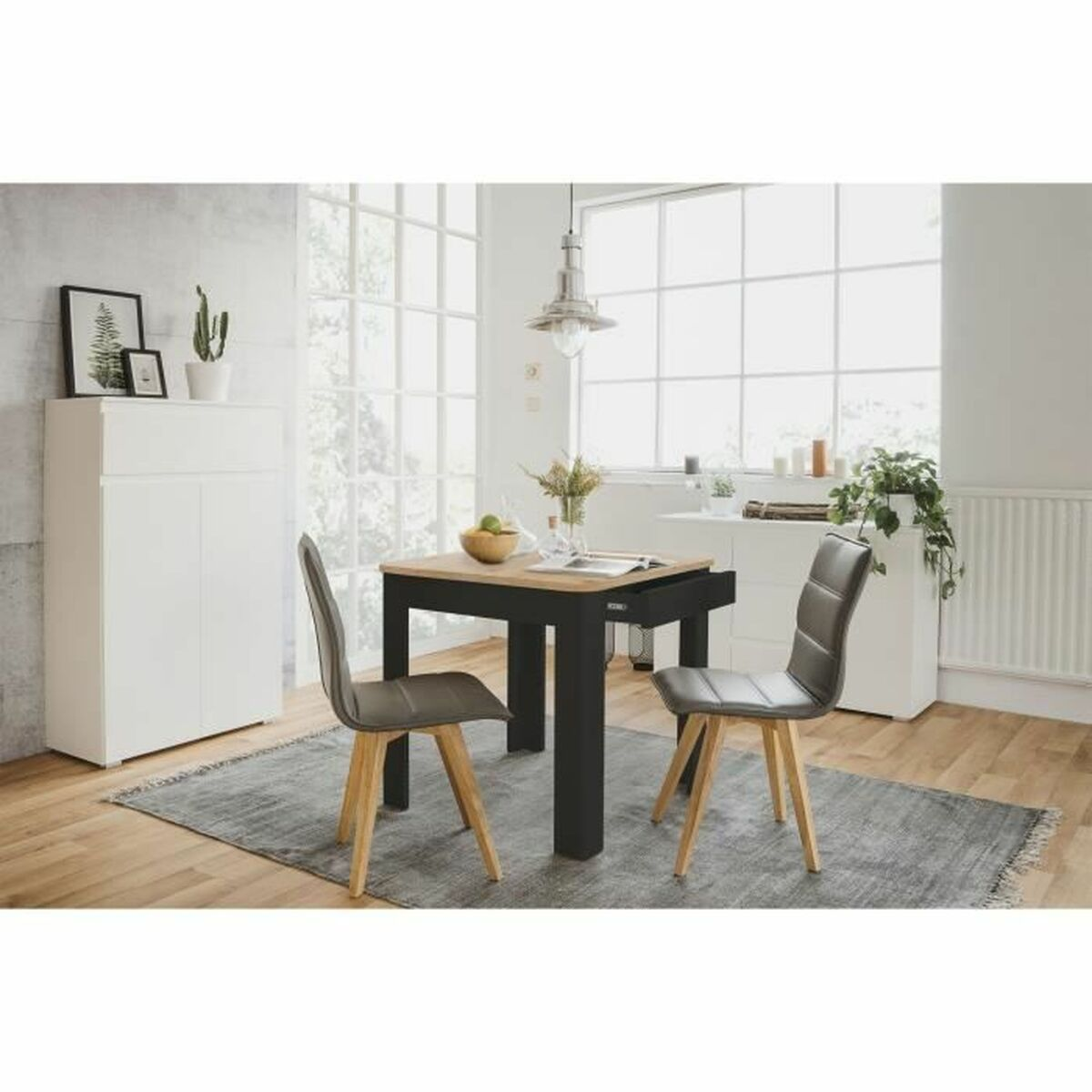 Esszimmer mit Tisch, Stühlen und Schrank. Ein Teppich und ein großes Fenster sind sichtbar. Der Raum hat natürliches Licht.