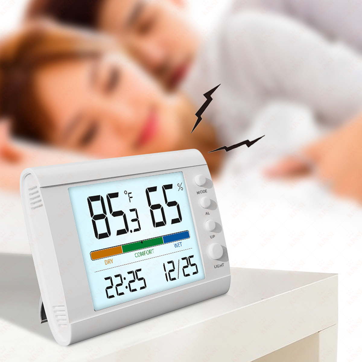 Ein weißes digitales Thermometer zeigt Temperatur und Luftfeuchtigkeit an. Im Hintergrund ist ein schlafendes Paar unscharf.