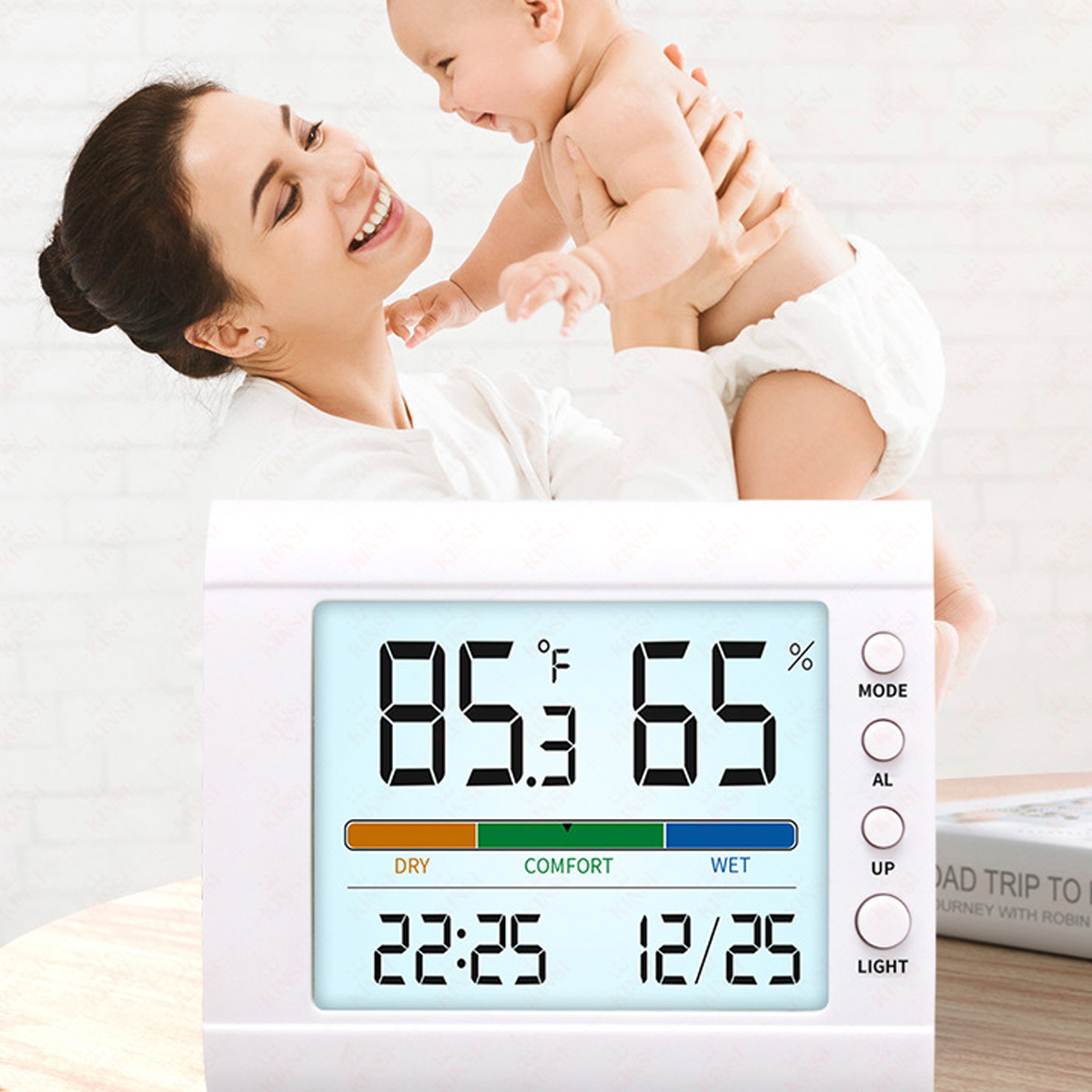 Eine lächelnde Frau hält ein Baby. Ein digitales Thermometer zeigt Temperatur und Luftfeuchtigkeit an. Die Szene deutet auf eine angenehme Umgebung hin.