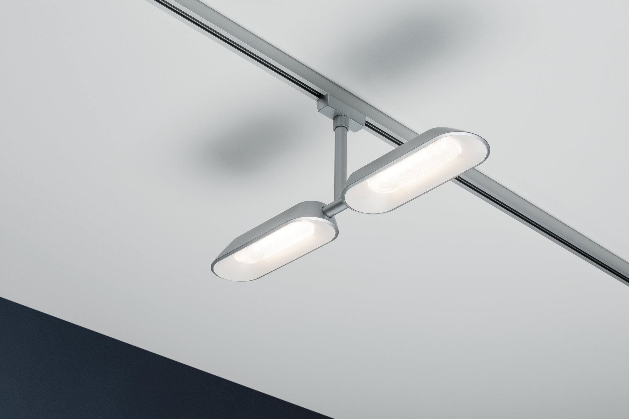 Due luci a LED argentate di forma ovale pendono da una rotaia su un soffitto bianco. Le luci sono illuminate, proiettando la luce verso il basso.