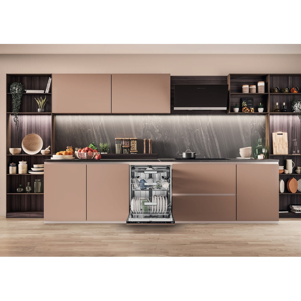 Cocina moderna con lavavajillas abierto. Los armarios son beige, la encimera gris. Varios objetos en estantes y mostrador. Suelo de madera.