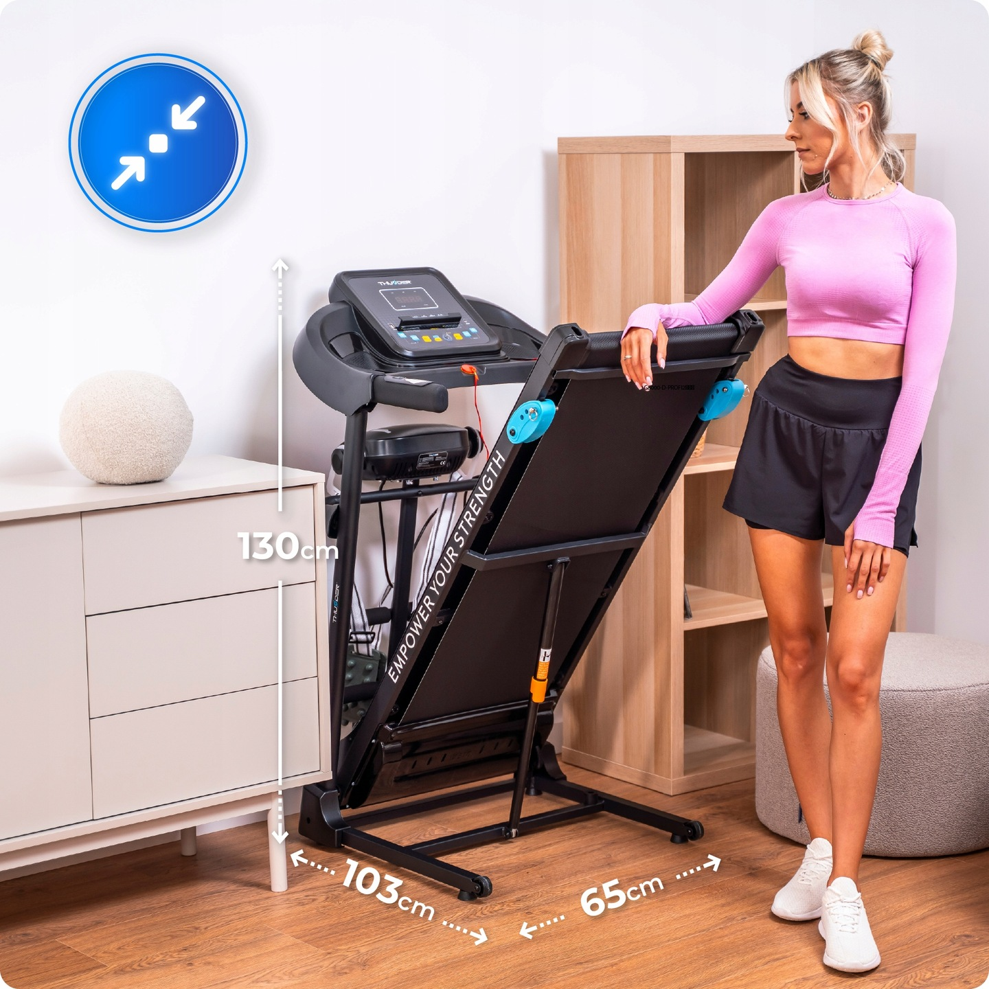 Blondynka obok pochylonej bieżni. Ma na sobie różowy top, czarne szorty i białe trampki. Pokazano wymiary.