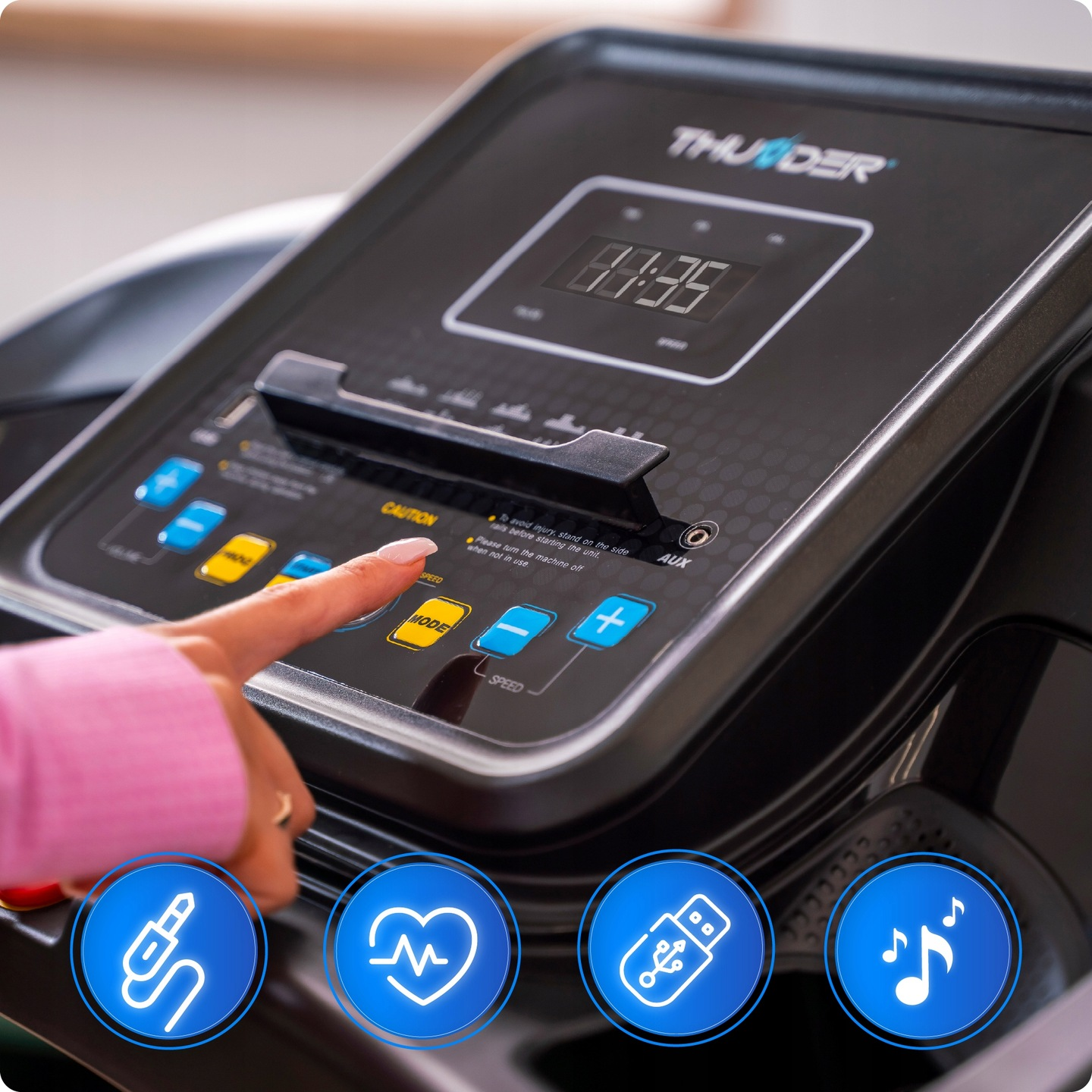 Ręka naciska przycisk na konsoli bieżni. Na ekranie widać 81:35. Widoczne są przyciski trybu i prędkości. U dołu znajdują się niebieskie ikony.