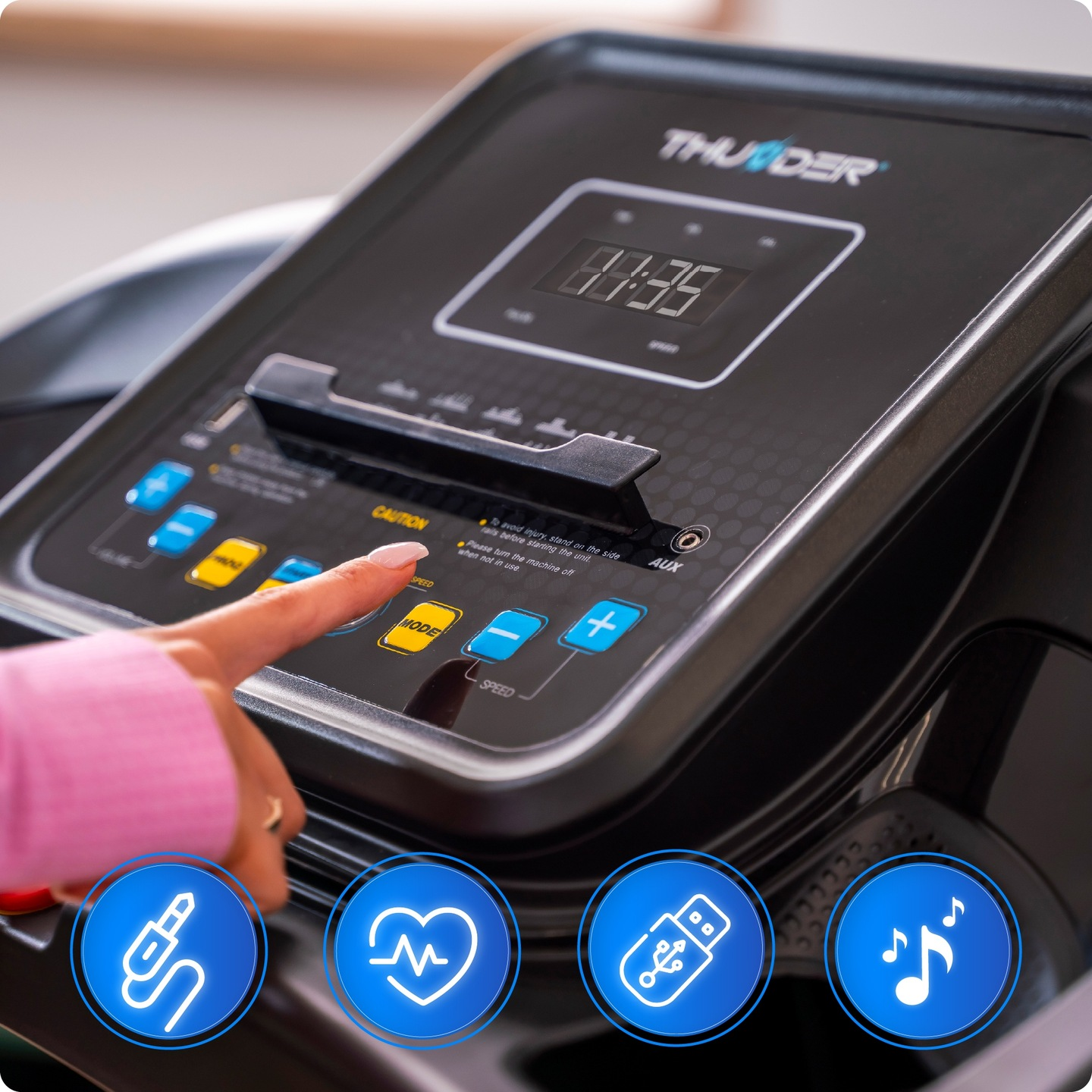 Palec naciska przycisk na konsoli bieżni. Konsola wyświetla czas. Widoczne ikony gniazda audio, serca, USB i muzyki.