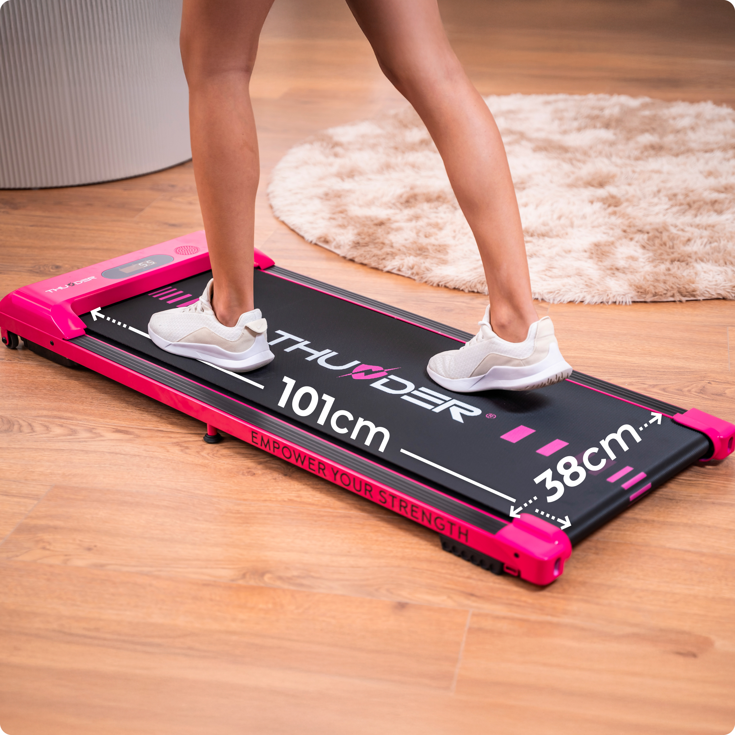 Osoba chodzi po różowo-czarnej bieżni. Podłoga jest drewniana. Dywan jest w tle.