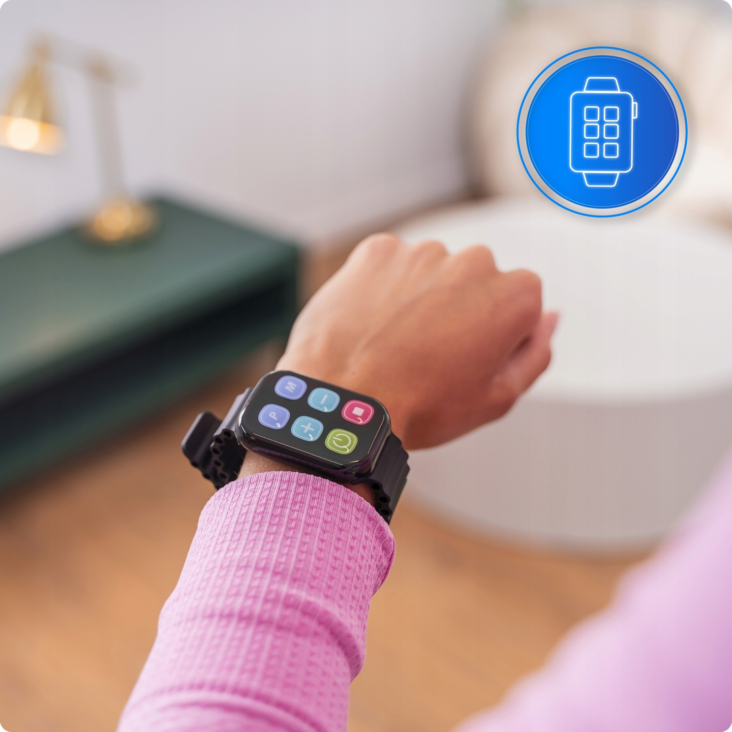 Osoba nosząca smartwatch z wieloma ikonami aplikacji na nadgarstku. Zegarek jest czarny, koszula różowa. Tło obejmuje meble.