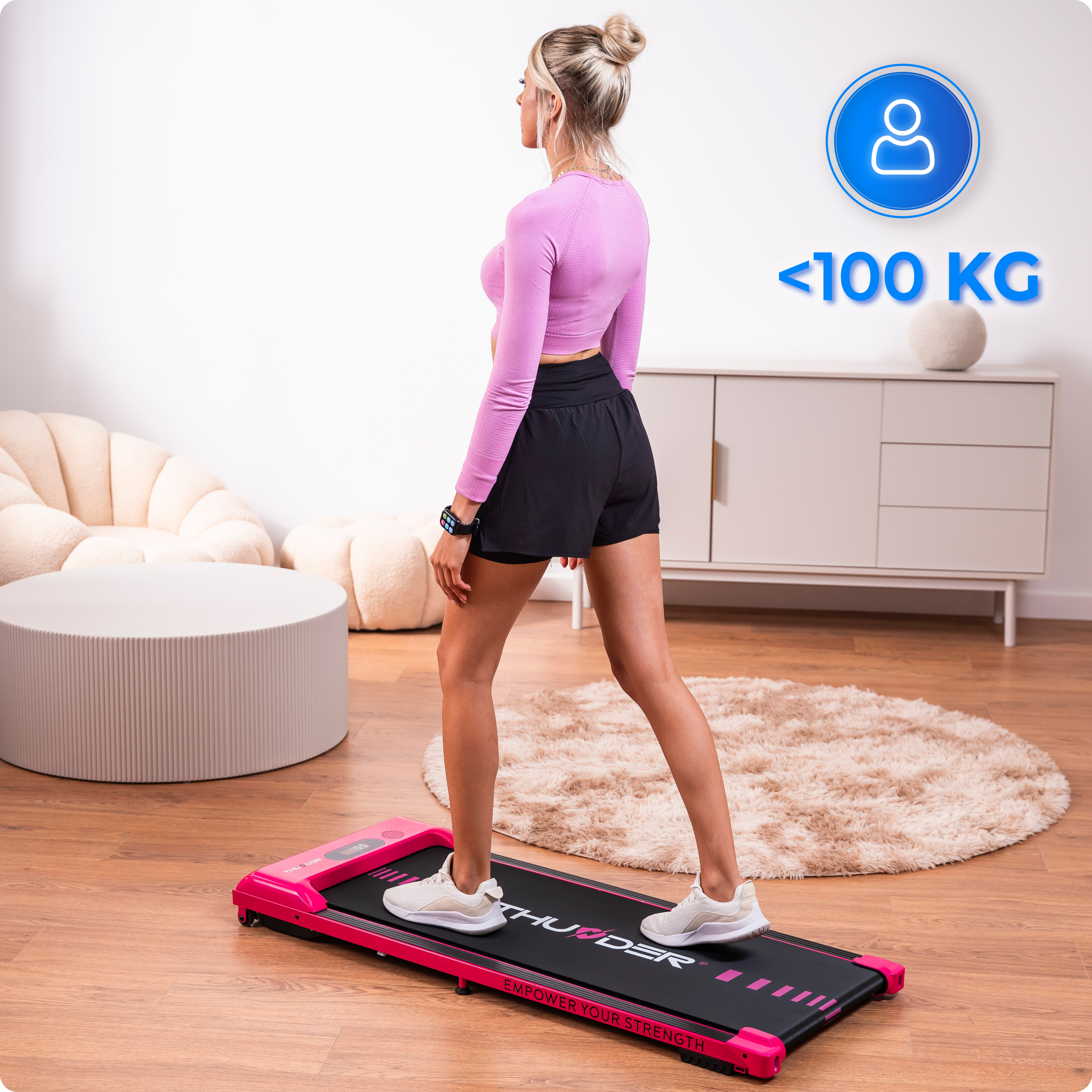 Kobieta korzysta z różowej bieżni. Ma na sobie różową koszulę i czarne szorty. Maksymalna waga to poniżej 100 kg.