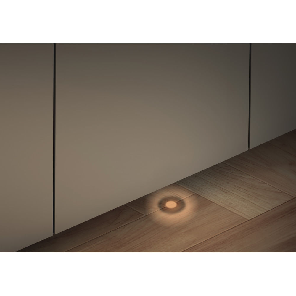 Una lampada da terra con un bagliore caldo illumina un pavimento in legno. Un muro è a sinistra. La luce è sul pavimento.