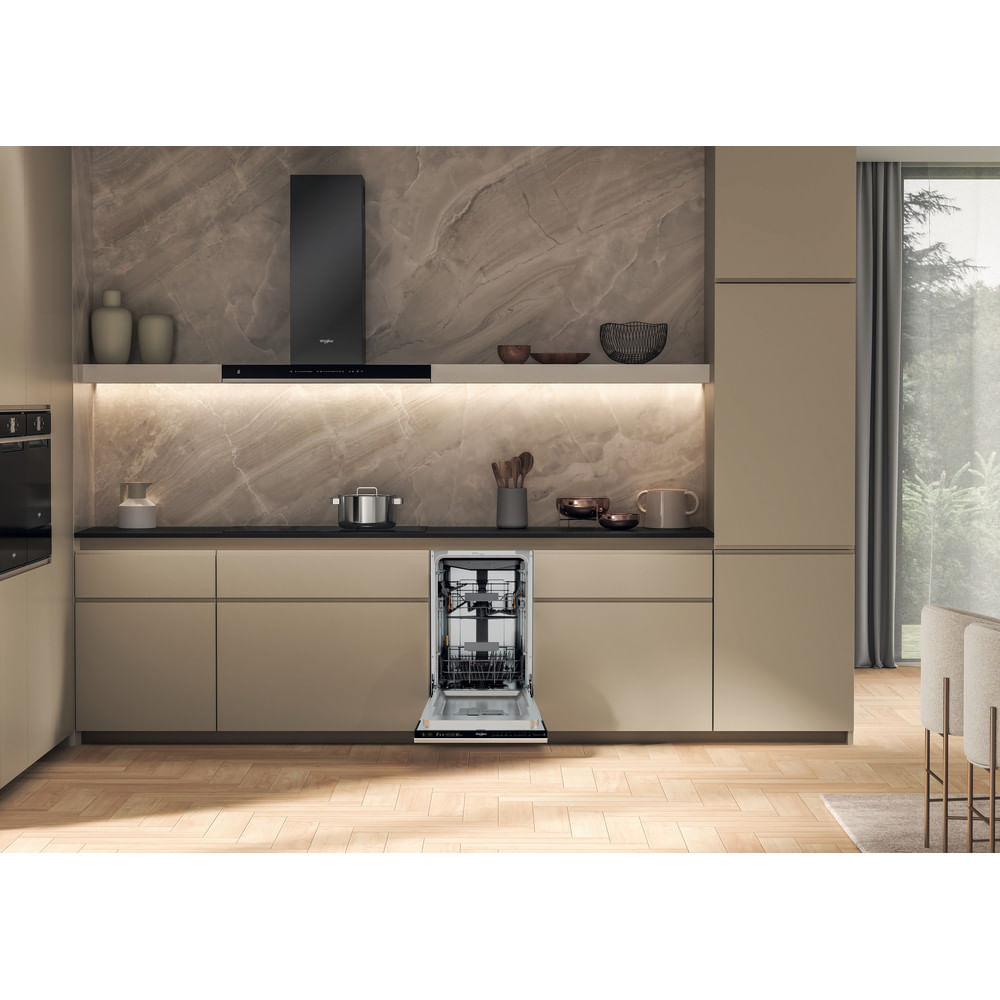 Cucina con lavastoviglie aperta. Armadietti beige e alzatina effetto marmo. Cappa nera e pavimento in legno. Vista di una finestra a destra.
