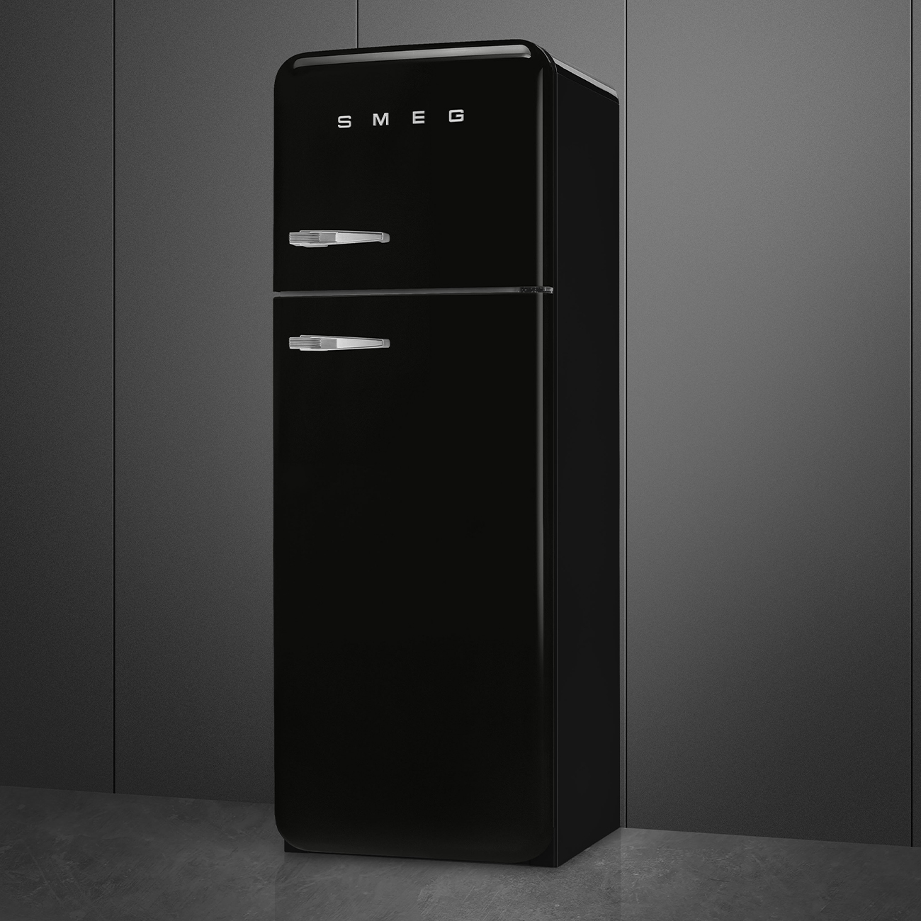 Un refrigerador SMEG negro se encuentra contra un fondo gris. Tiene dos puertas con manijas plateadas. El suelo es de hormigón gris.
