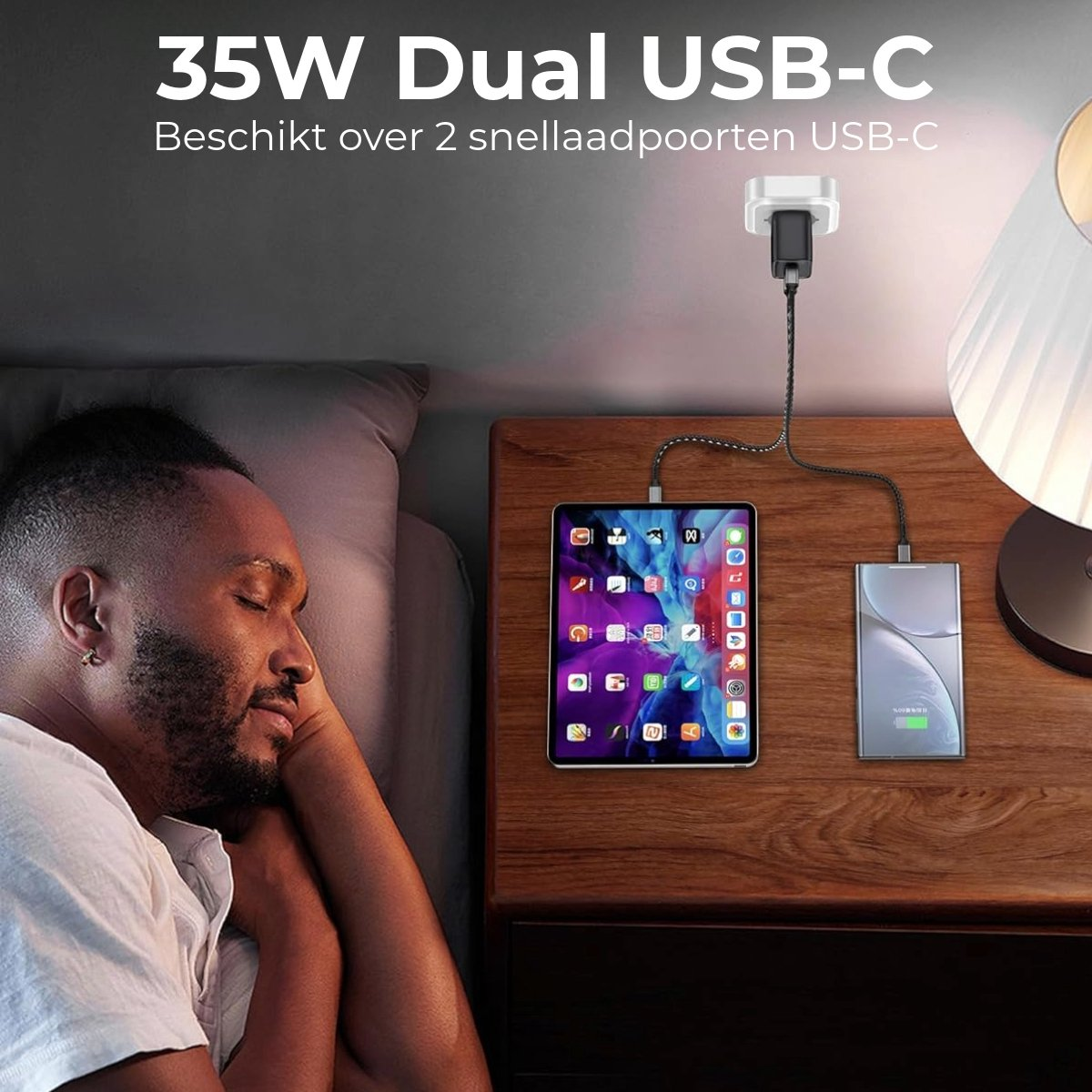 Man sleeping next to a nightstand with charging tablet and phone. A lamp is on the nightstand. Text says '35W Dual USB-C'.