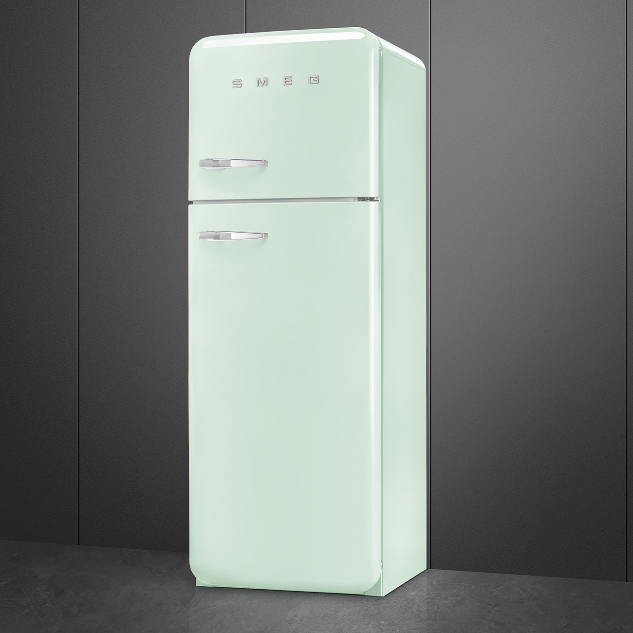 Un frigorifero Smeg verde chiaro è contro un muro grigio scuro. Ha due porte con maniglie argentate e il logo Smeg.