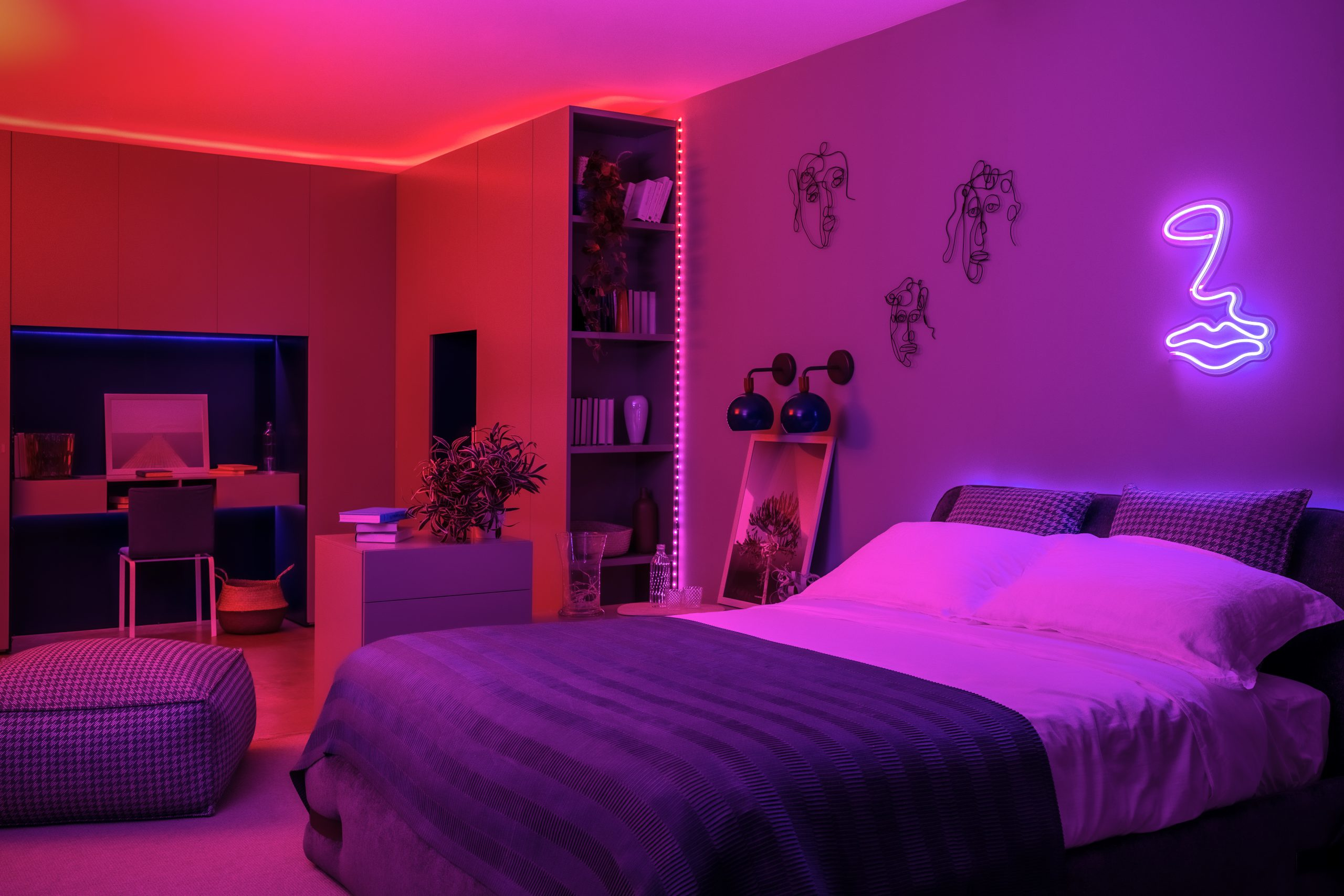 Sypialnia z fioletowym i czerwonym oświetleniem. Ma łóżko, stolik nocny i dzieła sztuki. Neonowe usta na ścianie.