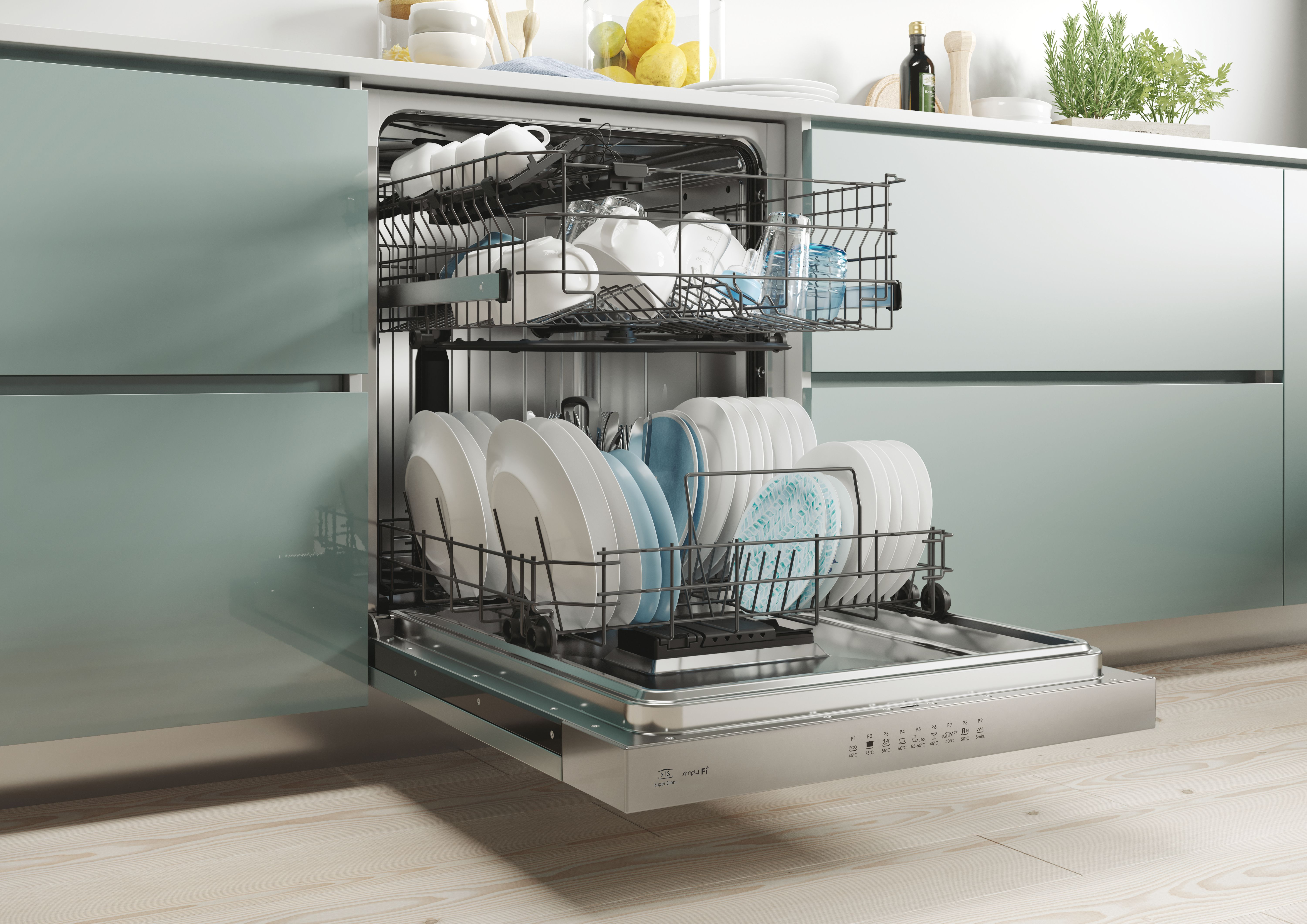 Lavastoviglie aperta con piatti puliti. Piatti e tazze bianche nei cestelli. Mobili da cucina verdi sullo sfondo.