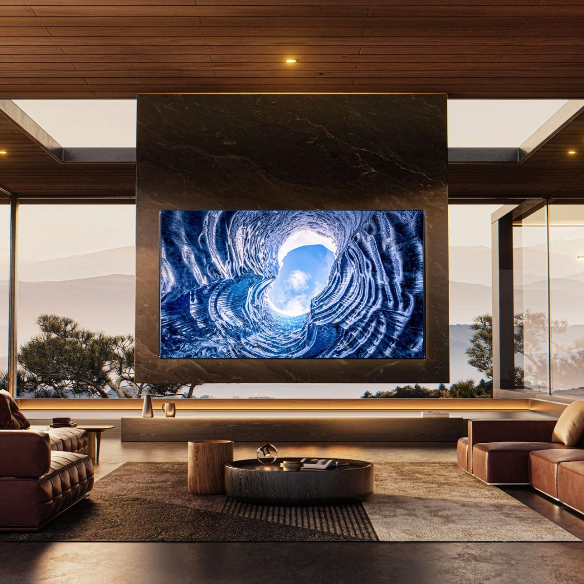 Wohnzimmer mit großem Fernseher, der eine Höhlenszene zeigt. Ledersofas, Holztisch und große Fenster mit Bergblick.