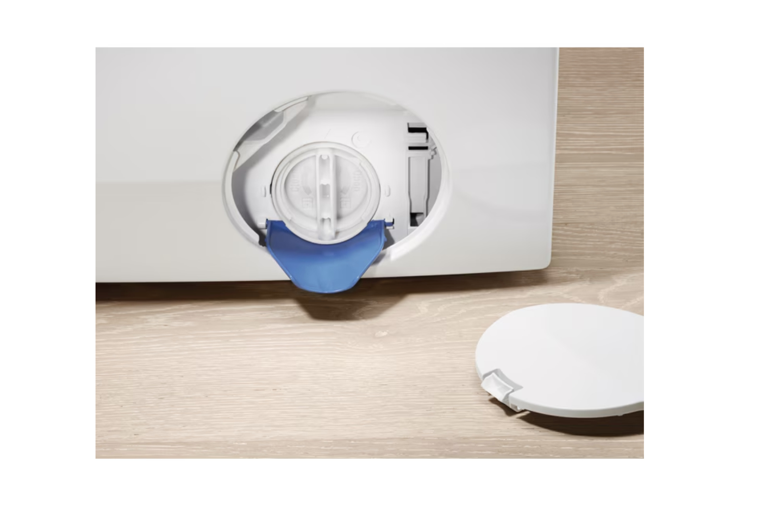 Filtr pralki. Biała pralka z niebieskim filtrem i białą nasadką na drewnianej powierzchni. Zbliżenie na komorę filtra.