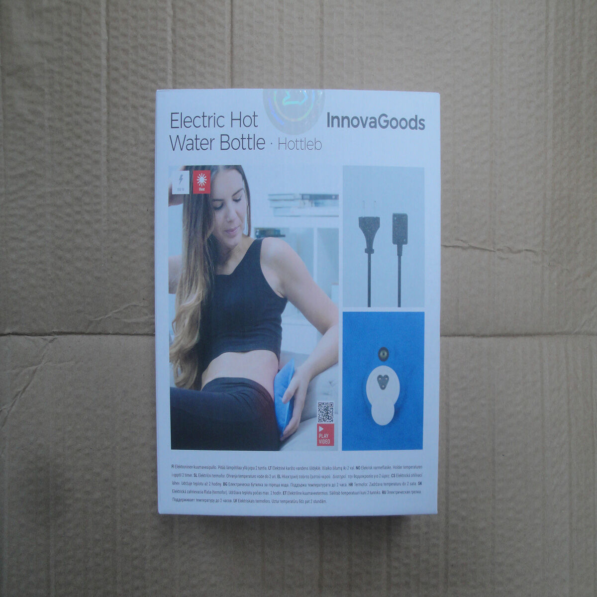 Pudełko elektrycznej butelki z gorącą wodą. Kobieta ją trzyma. Wyświetlane są szczegóły butelki i instrukcje.