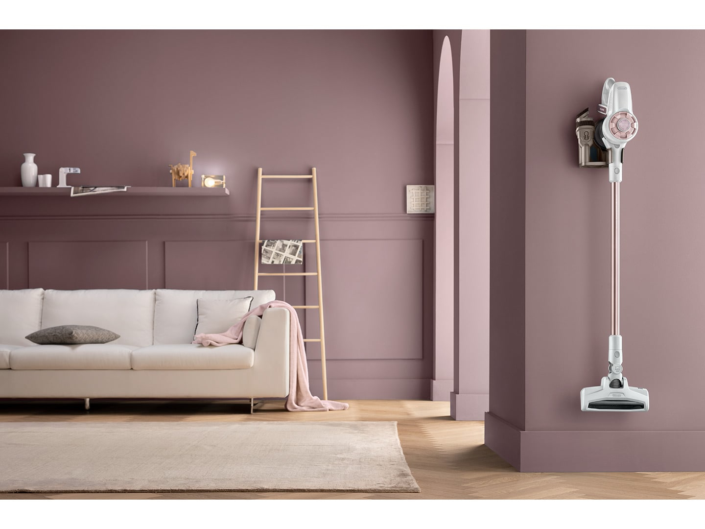 Un divano bianco, una scala in legno e un aspirapolvere sono in una stanza color malva. C'è un tappeto sul pavimento.