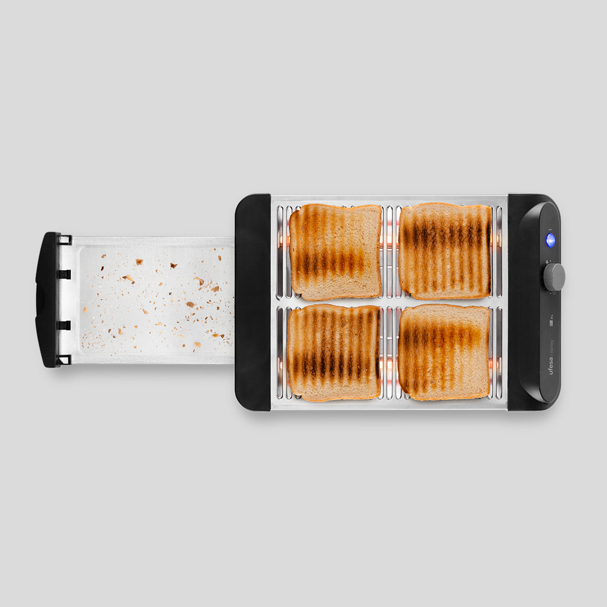 Un tostapane nero con quattro fette di pane tostato e un vassoio raccoglibriciole su sfondo grigio chiaro.