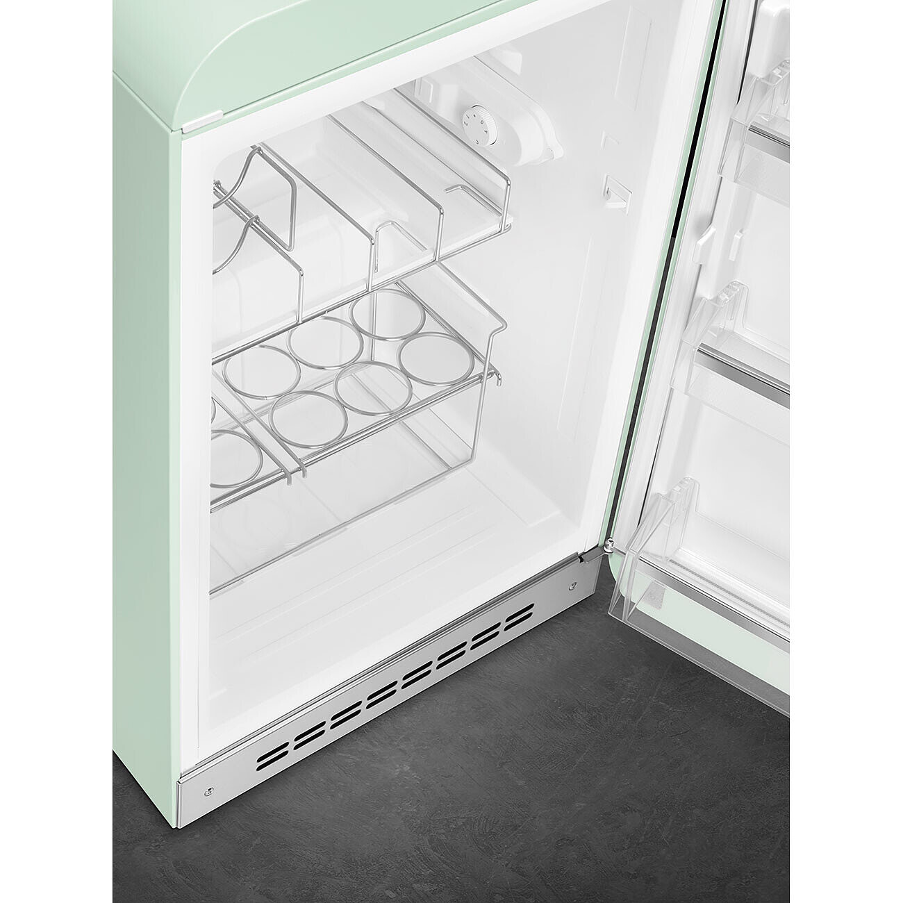 Un refrigerador retro verde menta con la puerta abierta. En el interior, tiene estantes y una rejilla de metal para guardar bebidas. La puerta está entreabierta.