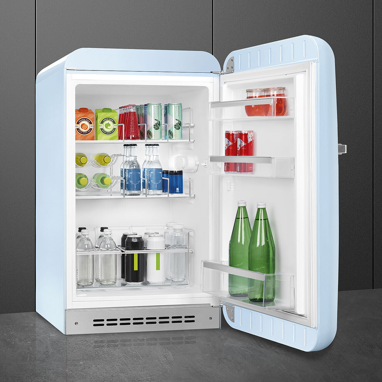 Un refrigerador retro azul claro está abierto, mostrando varias bebidas, incluyendo cajas de jugo, latas, botellas y frascos, todos ordenados.