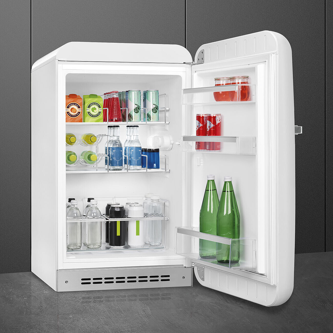 Un refrigerador retro blanco abierto, lleno de bebidas como cajas de jugo, latas, botellas y frascos. El interior es brillante, los artículos están organizados.