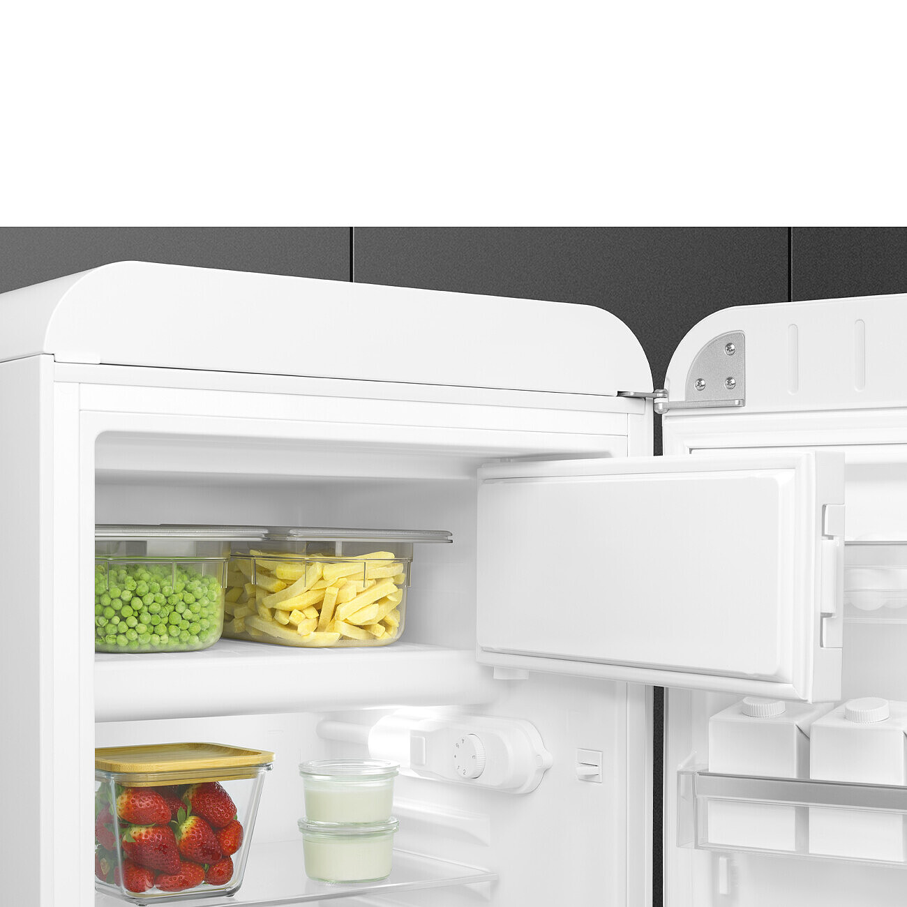 Refrigerador blanco abierto con comida dentro. Guisantes, patatas fritas, fresas, yogur. La puerta está abierta.