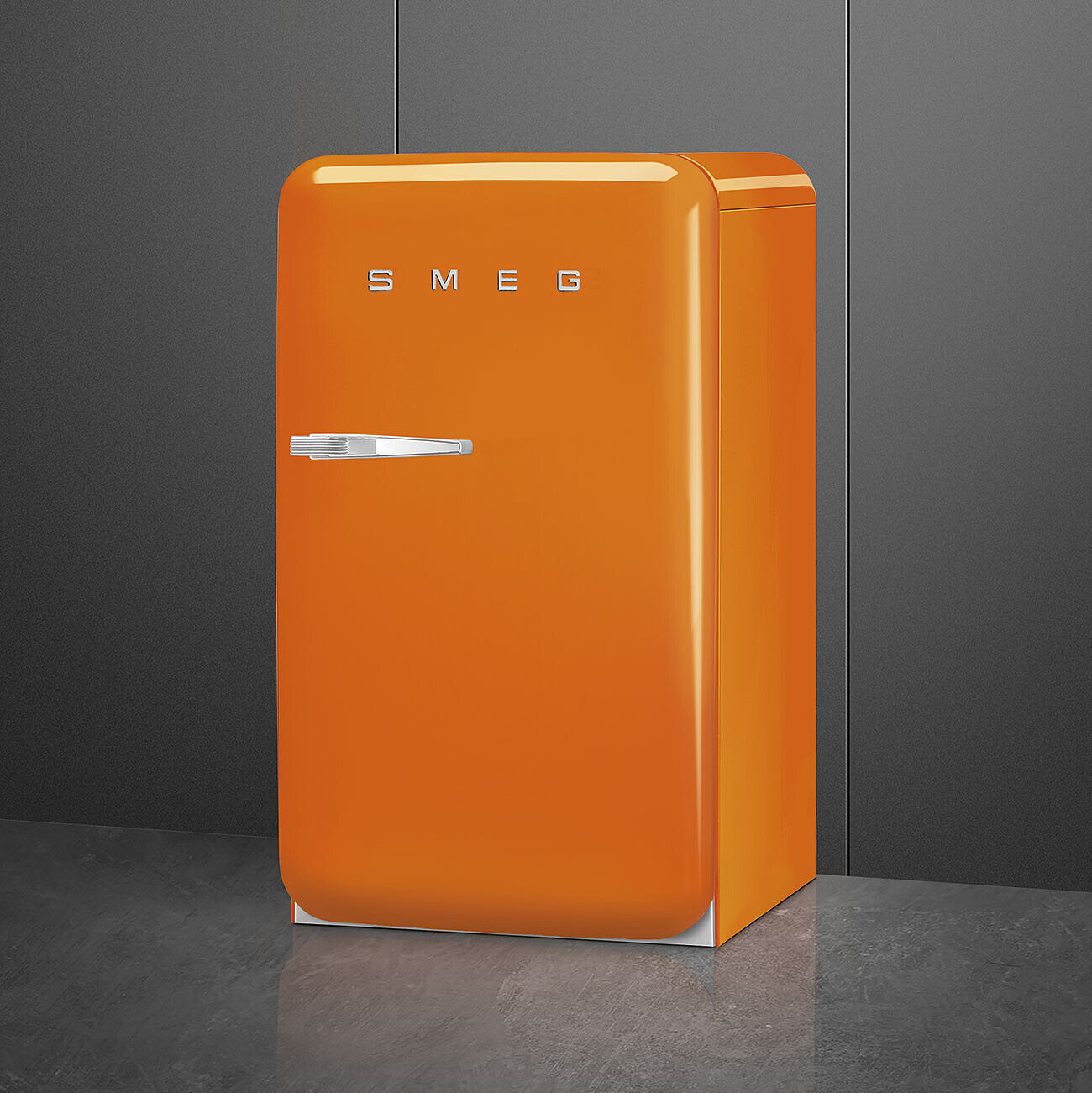 Un frigorifero SMEG arancione su un pavimento grigio. Lo sfondo è una parete grigio scuro.