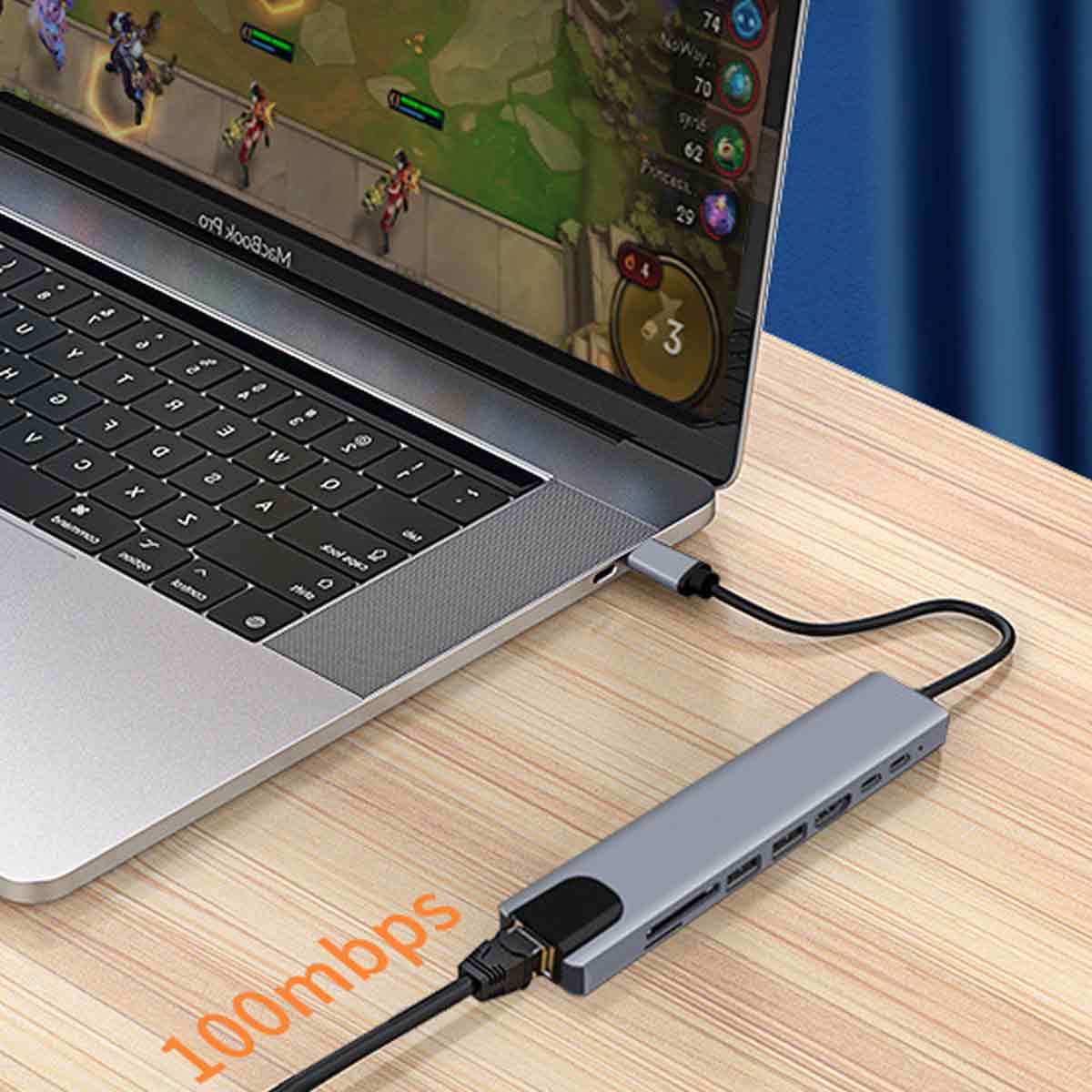 Laptop mit angeschlossenem Hub. Auf dem Bildschirm wird ein Spiel angezeigt, und 100 MBit/s stehen auf dem Holztisch.