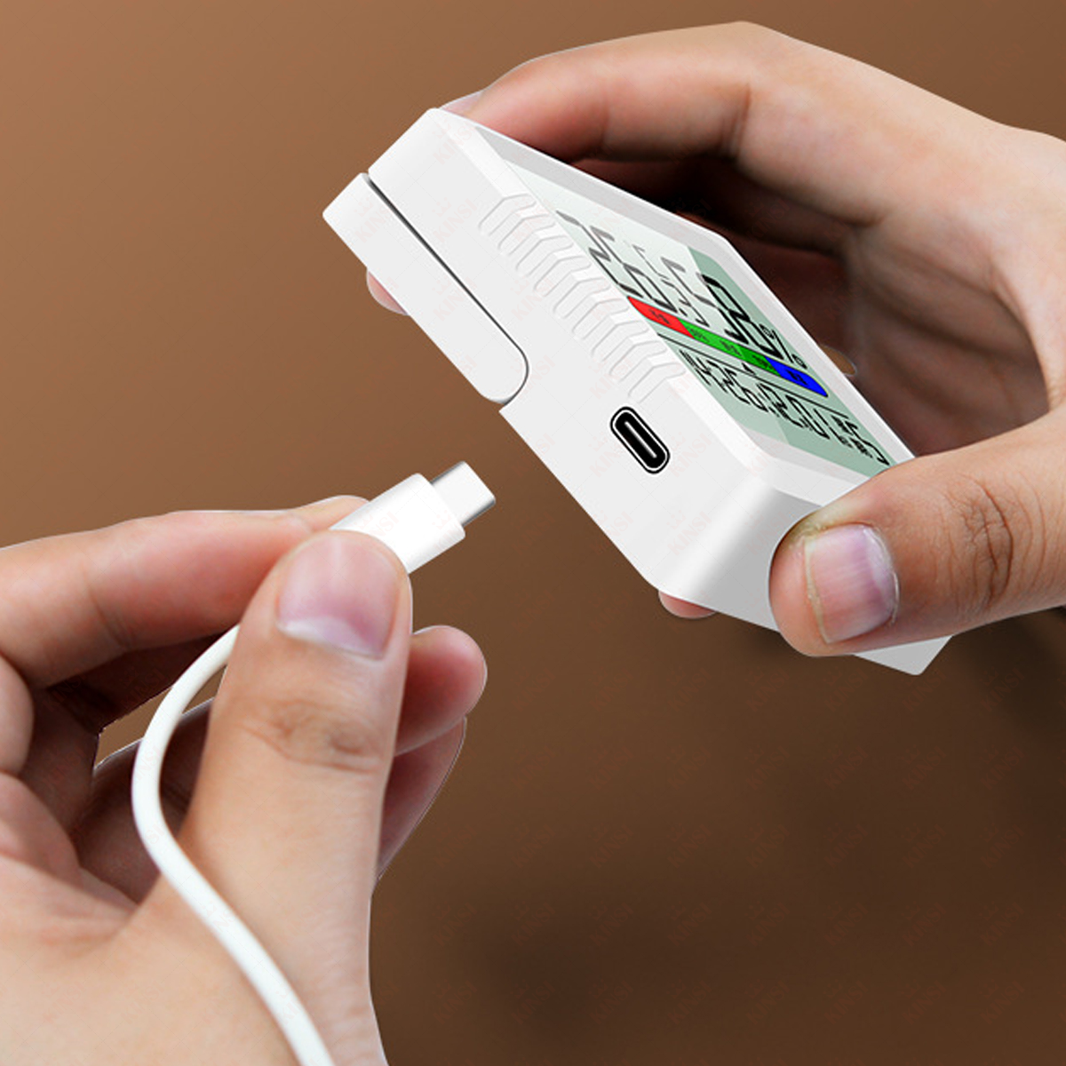 Hände halten ein weißes Gerät mit Bildschirm und stecken ein weißes USB-C-Kabel ein. Brauner Hintergrund.