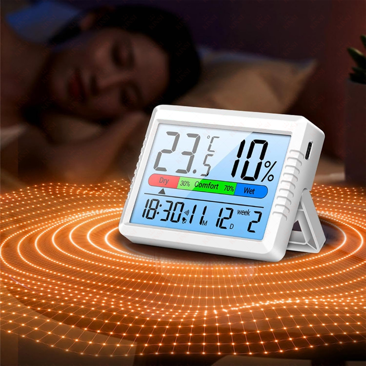 Ein digitales Thermometer zeigt Temperatur und Luftfeuchtigkeit in einem Schlafzimmer mit einer schlafenden Person im Hintergrund an.