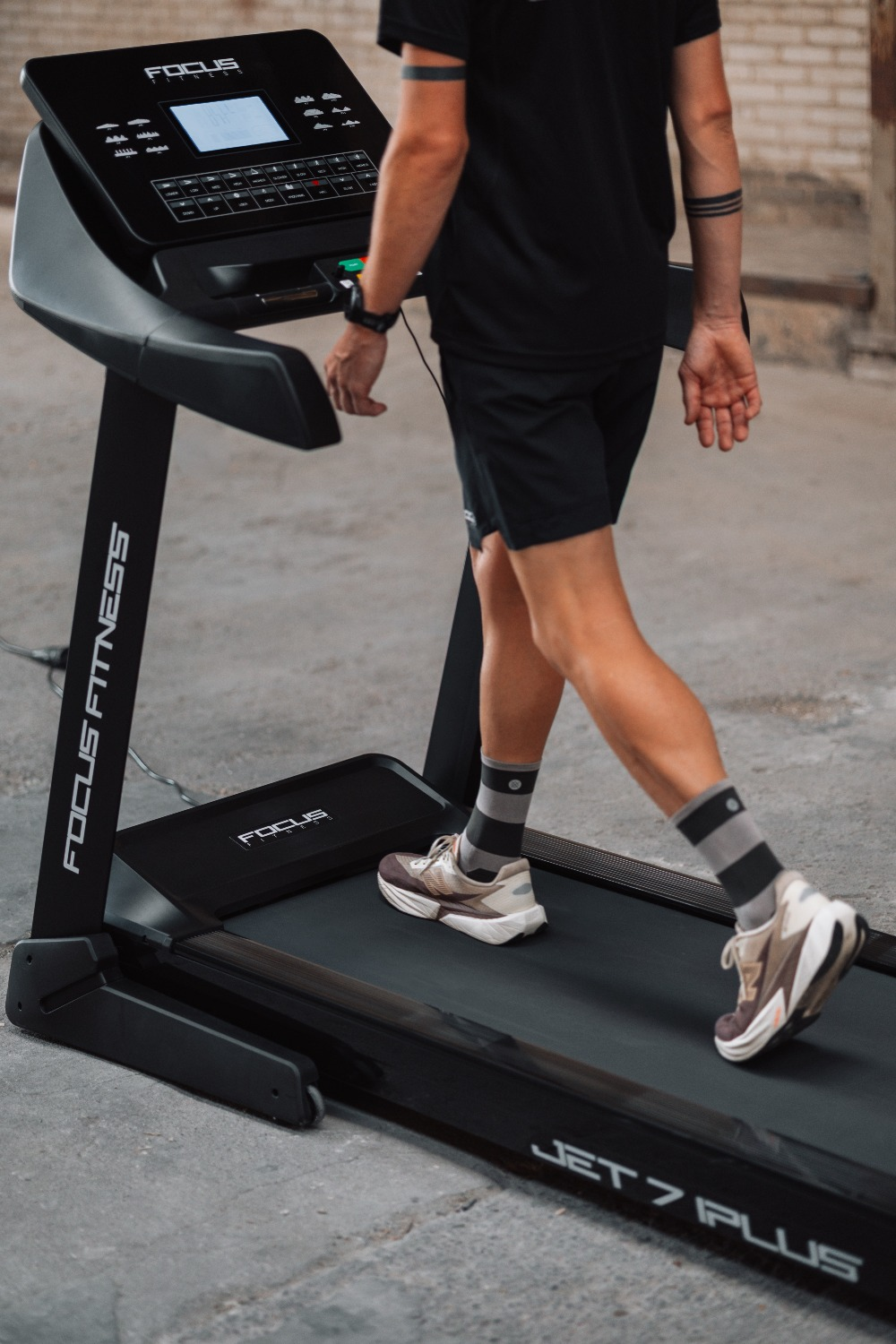 A person walks on a treadmill. They wear black shorts, a black shirt, and gray striped socks. The treadmill is black.