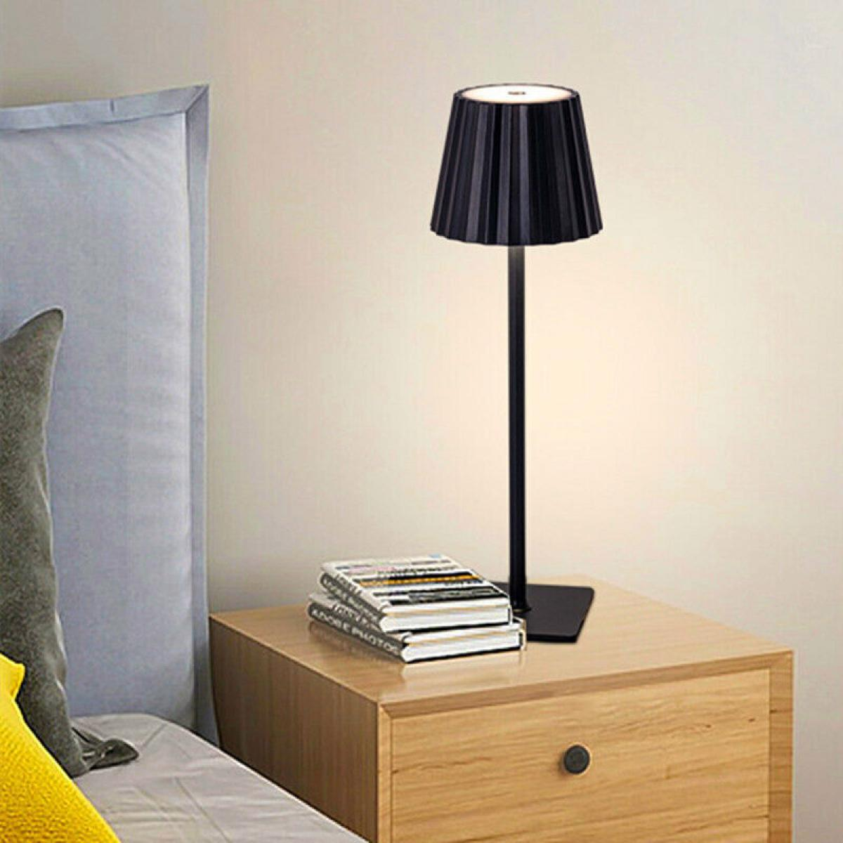 Eine schwarze Lampe steht mit Büchern auf einem Nachttisch aus Holz. Links befindet sich ein Bett mit grauem Kopfteil und Kissen.