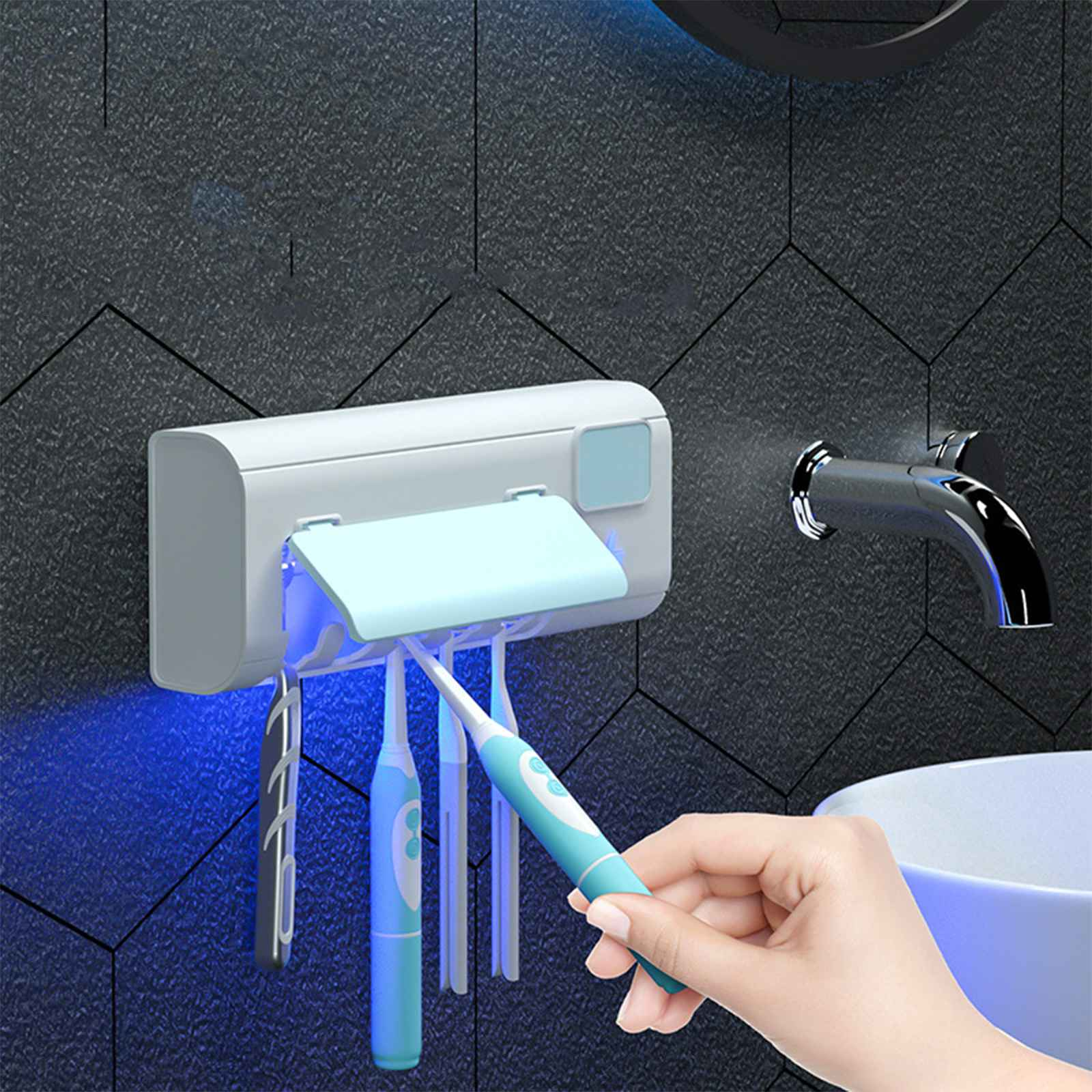 Eine Hand hält eine blaue Zahnbürste. Ein UV-Sterilisator mit Zahnbürsten hängt an einer Wand. Im Hintergrund sind ein Wasserhahn und ein Waschbecken.